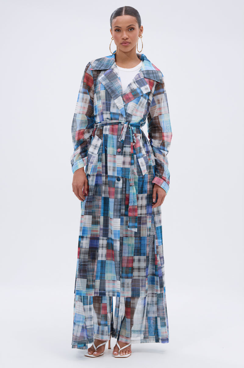 A woman wears the LIVING THE LIFE PLAID MESH TRENCH—a lightweight, colorful plaid mesh layer—belted at the waist over a white top and pants, styled with hoop earrings and white heeled sandals, standing against a plain white background. 2
