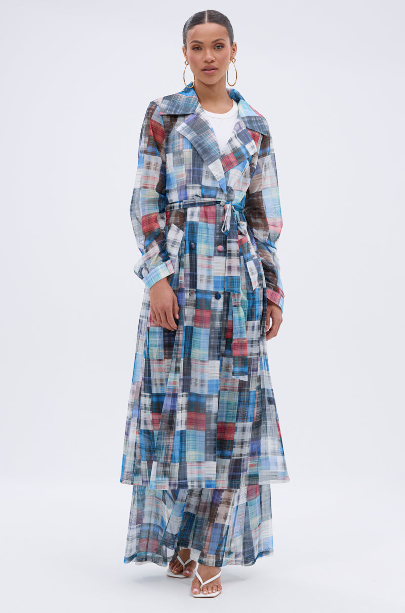 Wearing the LIVING THE LIFE PLAID MESH TRENCH over a white top and skirt, accessorized with hoop earrings and white heeled sandals, a person stands against a plain white background. 3