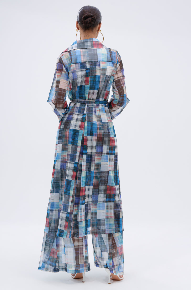 A woman faces away, wearing the LIVING THE LIFE PLAID MESH TRENCH as a lightweight layer over wide-leg multicolor plaid pants. Her hair is in a bun, and she finishes the look with large hoop earrings and heeled sandals. 7