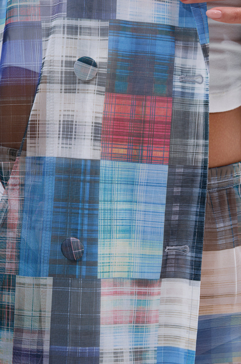 Close-up of the LIVING THE LIFE PLAID MESH TRENCH, showcasing its vibrant multicolor plaid pattern with blue, red, white, and yellow hues, buttons and buttonholes. A hand rests near the top edge, partially revealing a white shirt underneath. 8