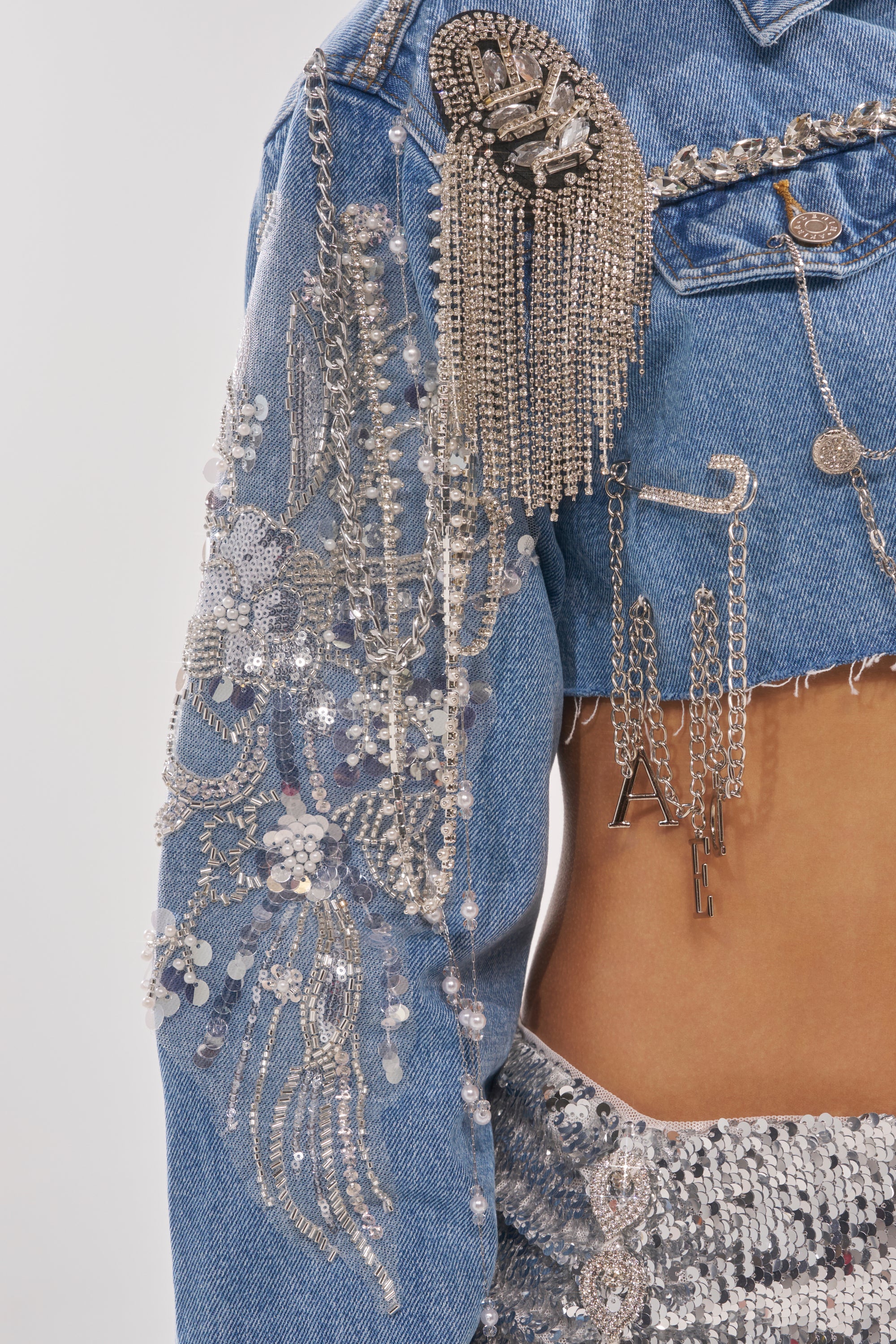 A close-up of the PIPER EMBELLISHED DENIM JACKET, featuring silver chains, sequins, and bead detailing, styled over a bare midriff with a silver sequin skirt. 14