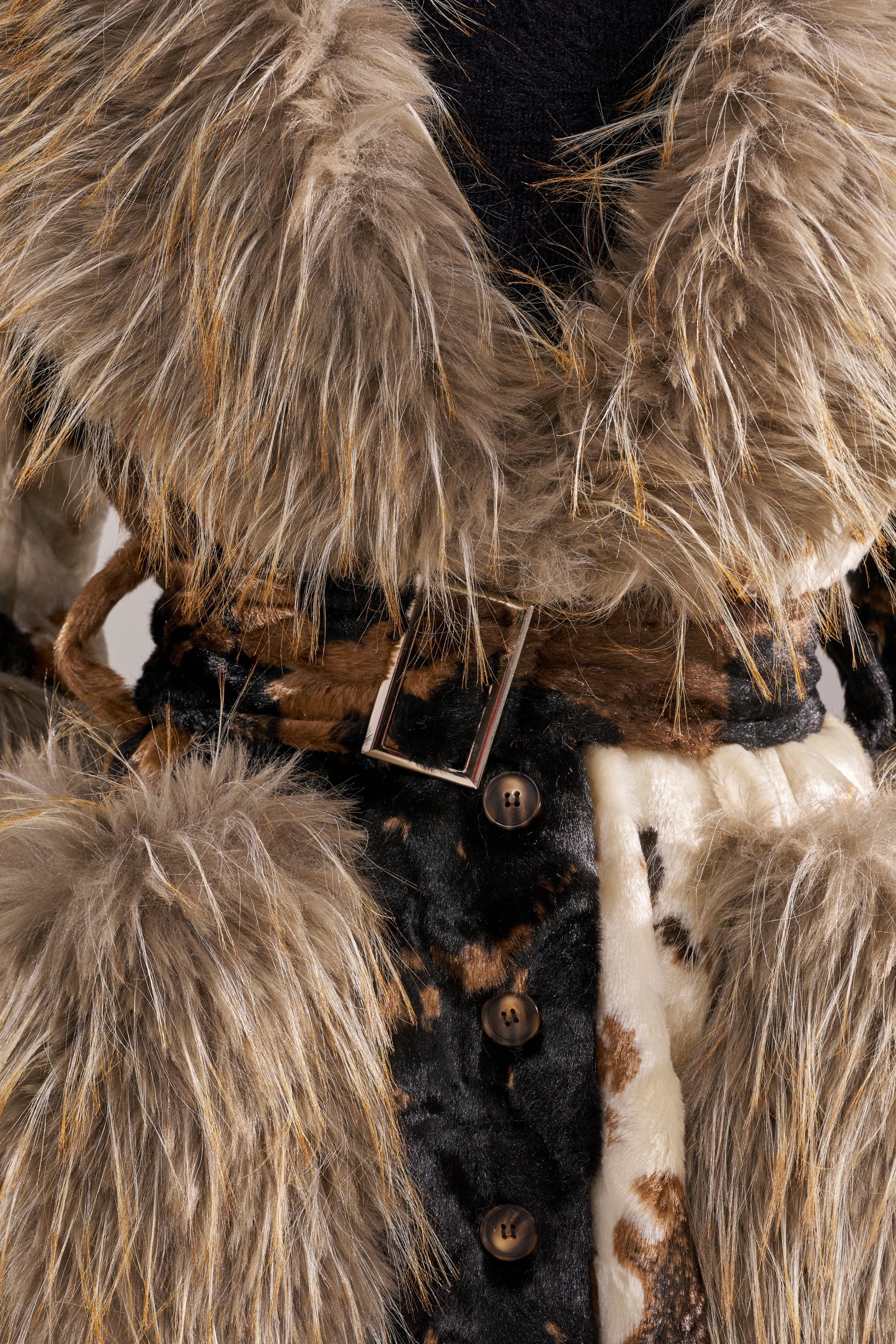 Close-up of the FREYA FUR TRIM TRENCH, a faux fur trench coat with shaggy brown and beige textures, subtle animal print, black buttons, and a brown belt with a silver buckle at the waist.