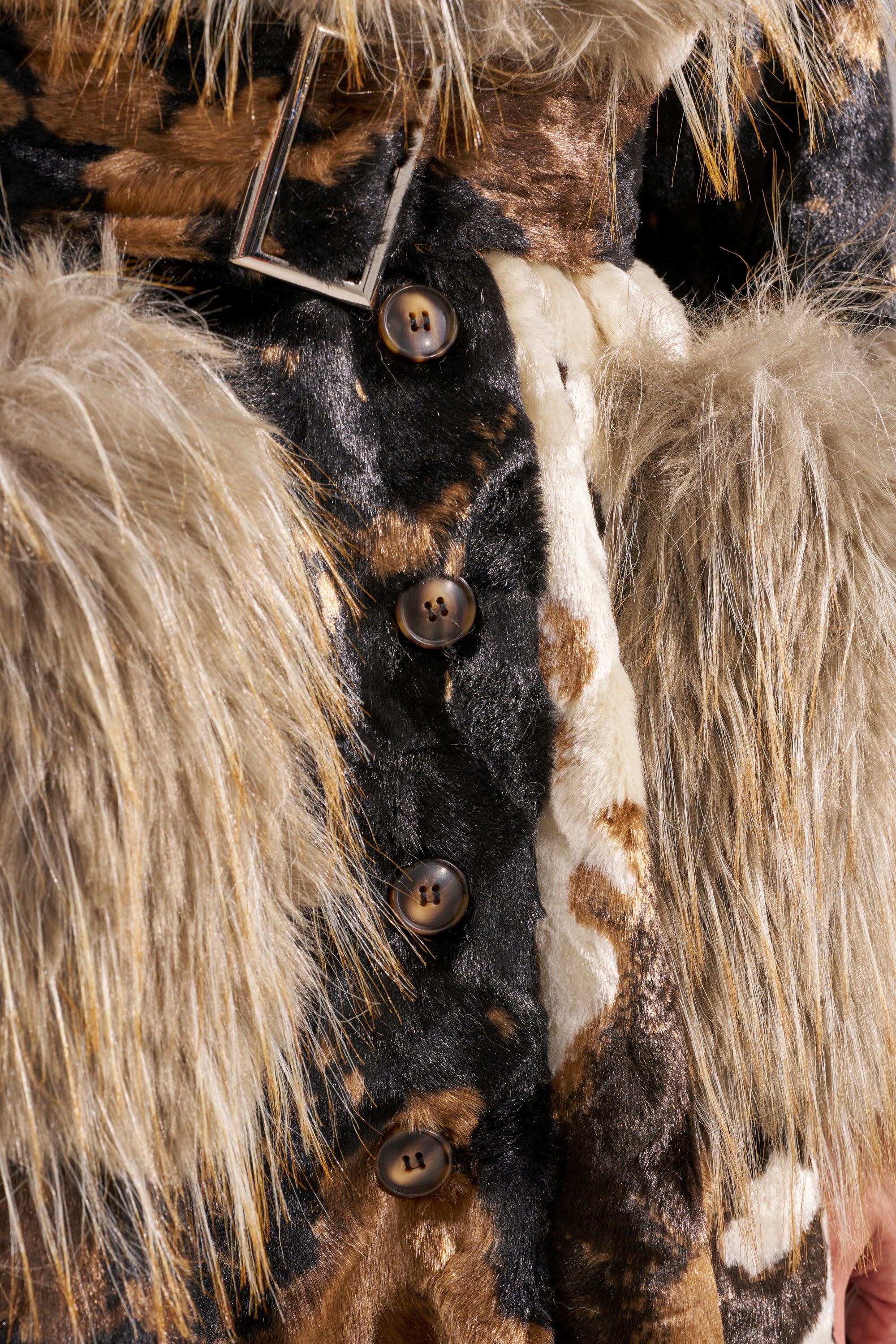 Close-up of the FREYA FUR TRIM TRENCH, a faux fur trench coat with multicolored brown, cream, and black shaggy fibers, large buttons, and a silver rectangular buckle.