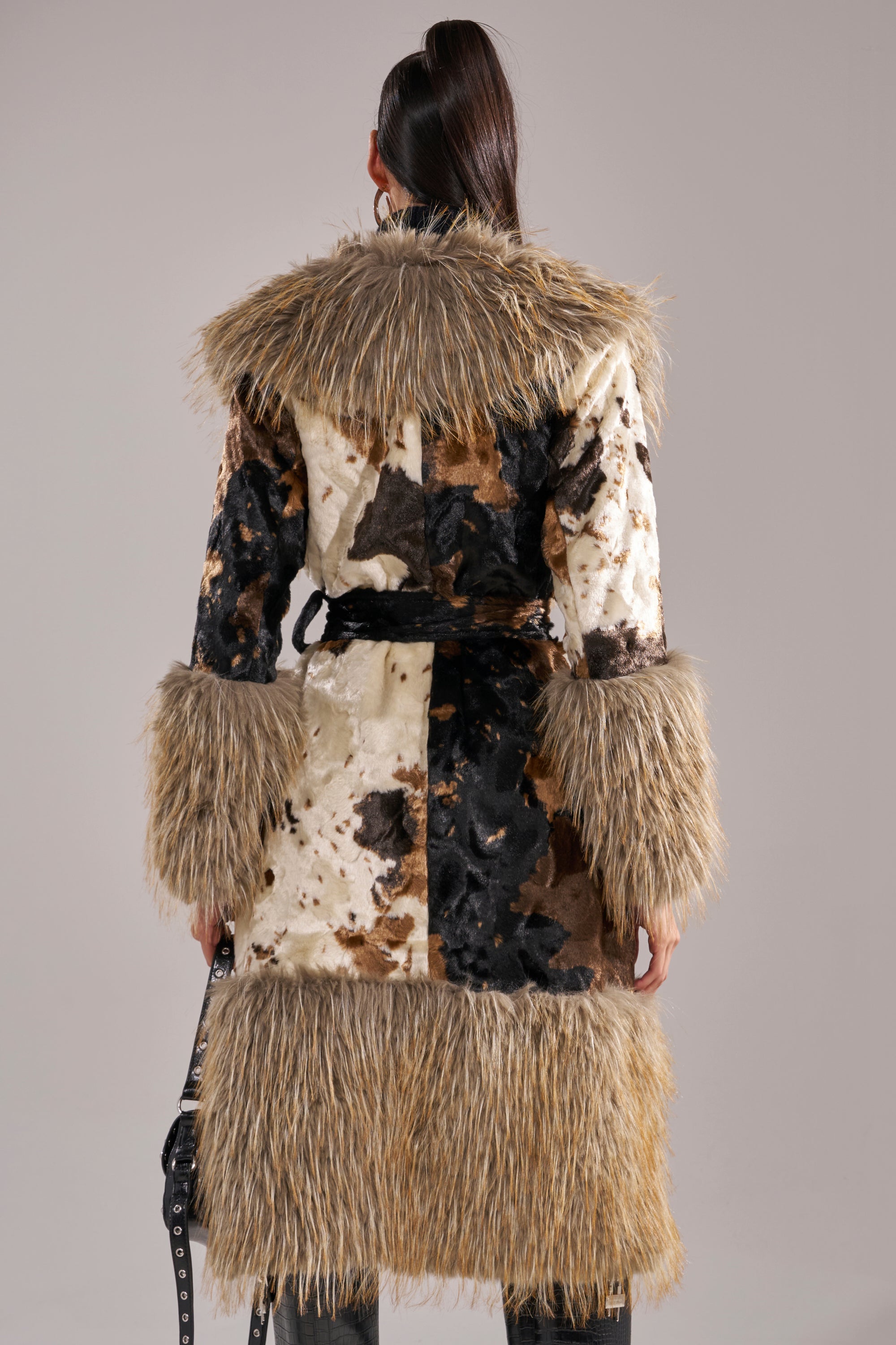 Wearing the FREYA FUR TRIM TRENCH, a person stands with their back to the camera; the longline coat features patchwork faux fur and shaggy trim on the collar, cuffs, and hem against a neutral background.