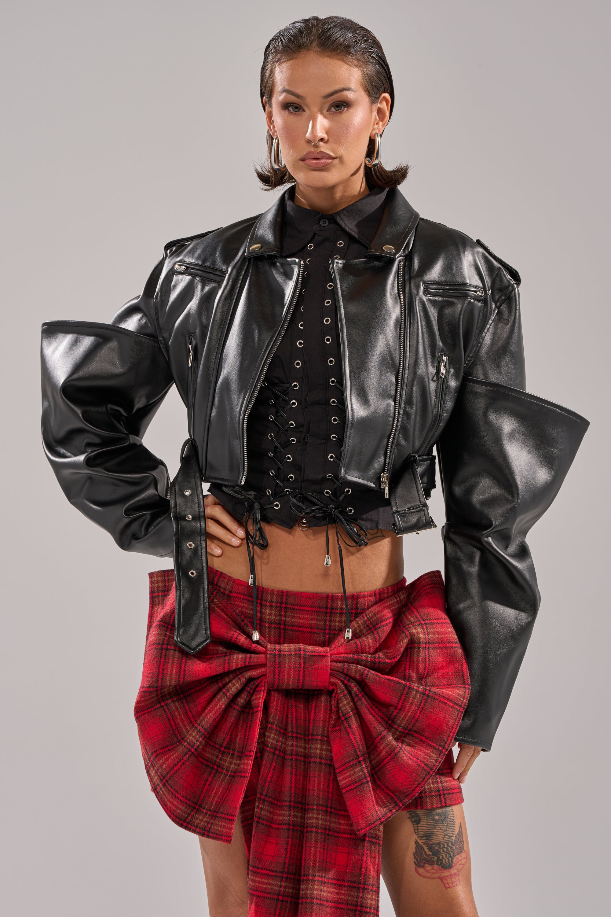 Wearing the STACK IT UP CROPPED MOTO over a lace-up top and red plaid skirt with a big front bow, a person with short, slicked-back hair stands confidently against a plain light background. 2