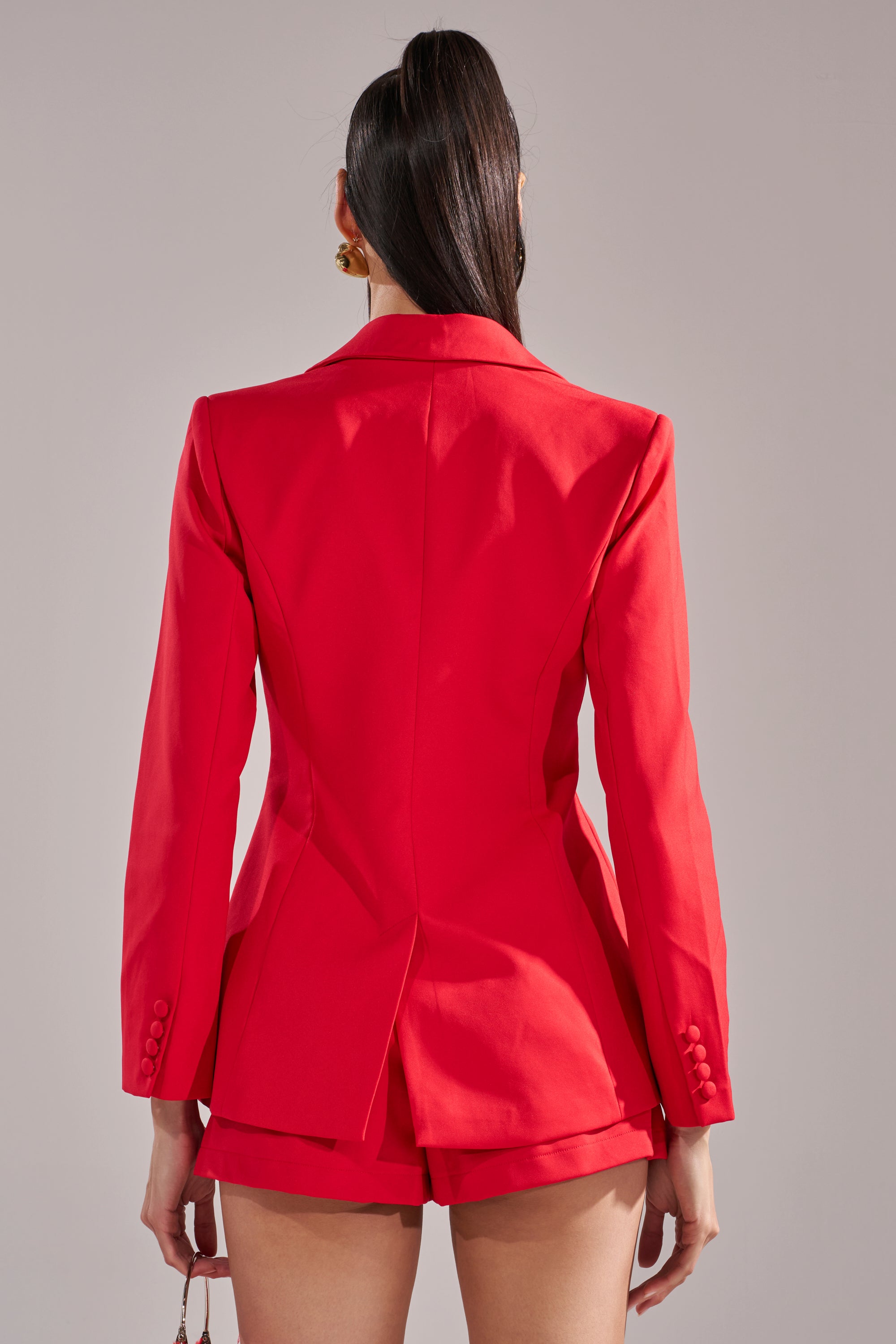 A person with long dark hair in a high ponytail models the CHERRY BOMB BLAZER, paired with matching shorts, as seen from the back against a plain light gray background. 4