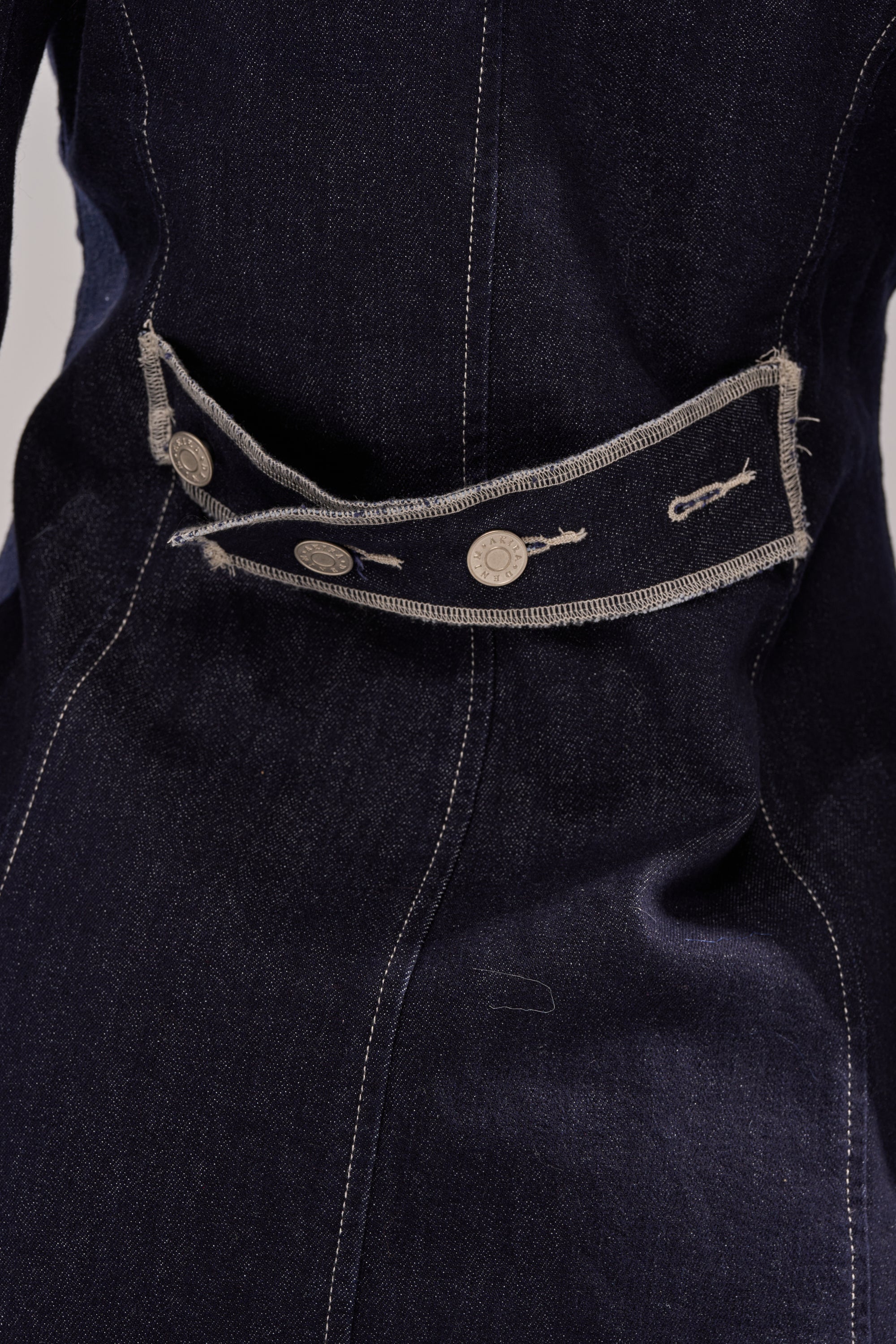 Close-up of the JESSE DENIM BLAZER, featuring dark denim with beige stitching, a decorative belt strap with metallic buttons and embroidered key designs, highlighting modern tailoring and a refined, structured silhouette. 10