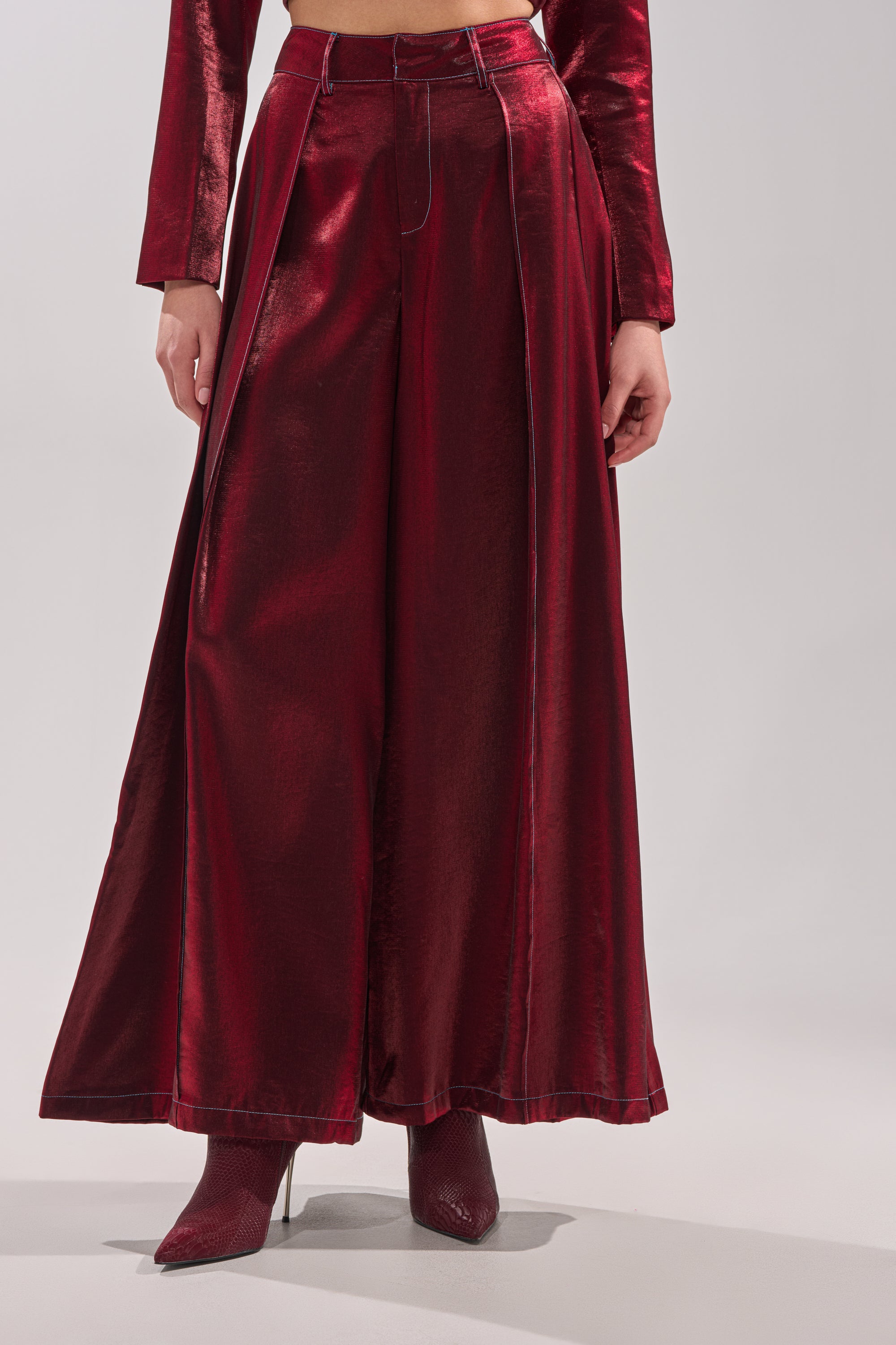 A person stands against a light gray background wearing the shiny red MISS YOU MOST WIDE LEG PANT, a matching long-sleeve top, and pointed ankle boots. 0