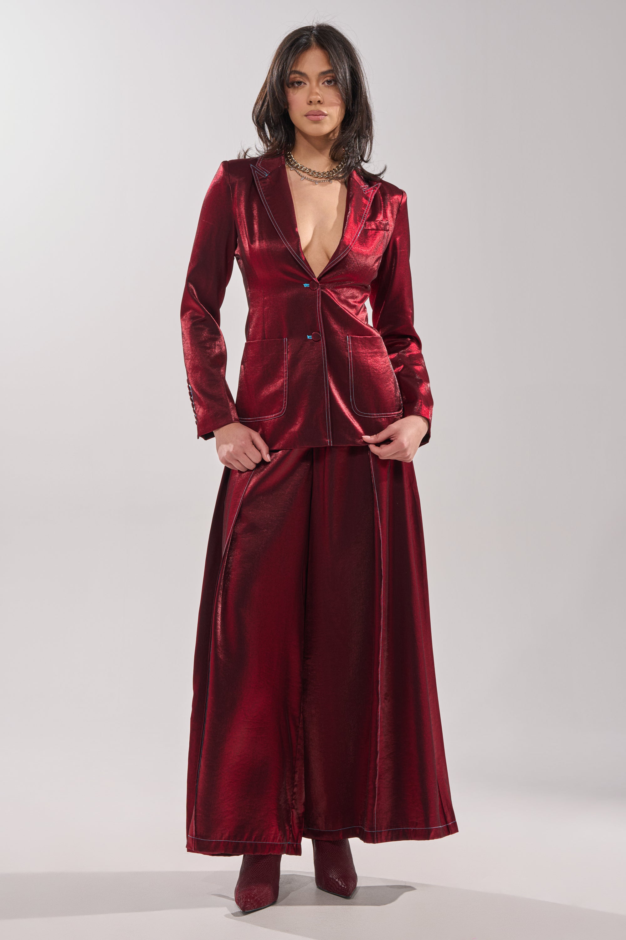 A woman faces forward in a deep red satin pantsuit, featuring the MISS YOU MOST WIDE LEG PANT and matching boots, set against a plain light gray background. 3