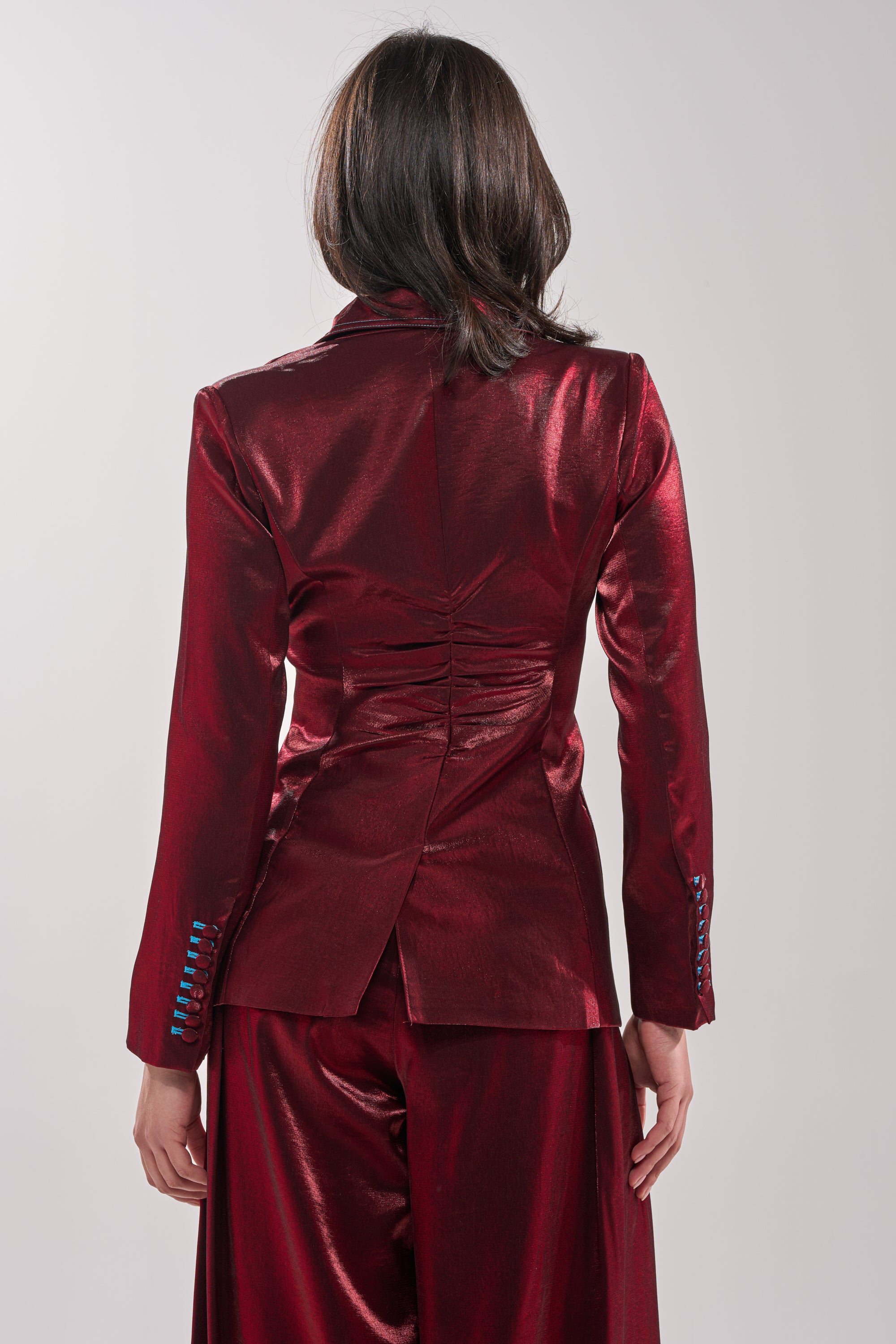 A person with medium-length brown hair is shown from the back, wearing the MISS YOU MOST BLAZER in shiny deep red satin-finish with matching pants, against a plain light background. 3