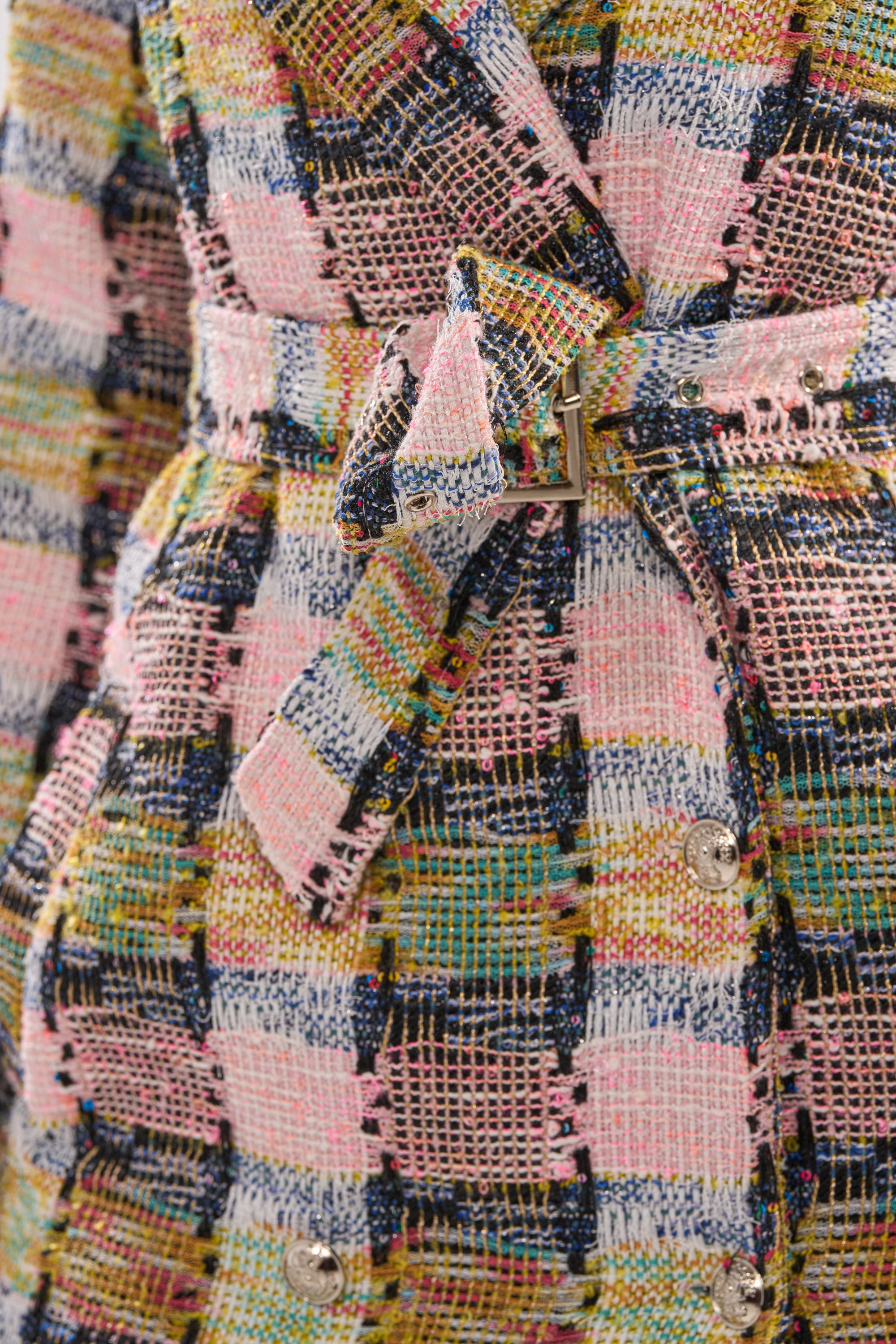Close-up of the MAIN SQUEEZE TWEED TRENCH, a pastel check coat in textured, multicolored fabric with pink, blue, yellow, and green threads, featuring a matching waist belt and shiny round buttons for a chic look. 7