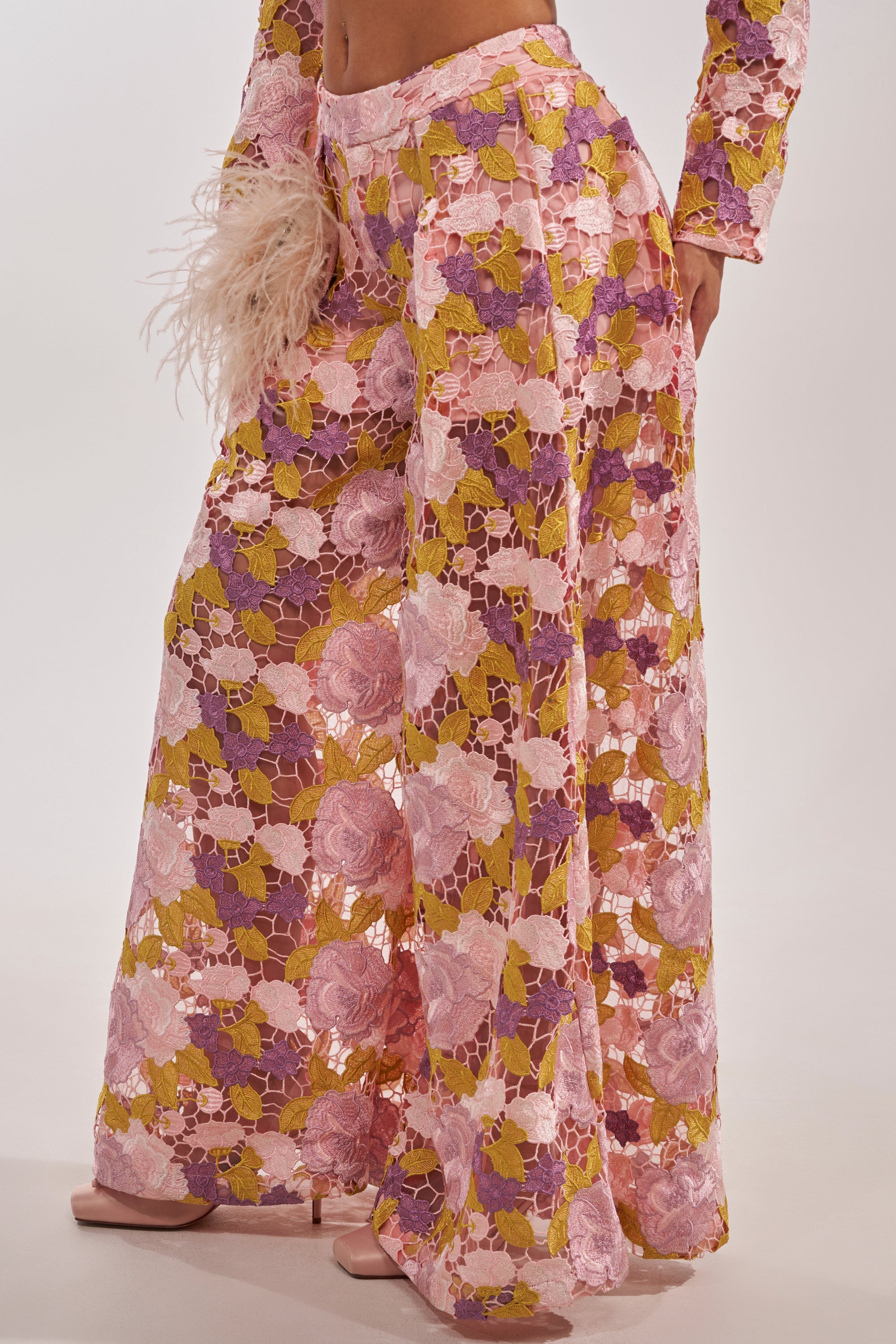 Wearing LILA LACE PANT, vintage luxe wide-leg trousers crafted from sheer, lace-like fabric with pink, purple, yellow, and white floral patterns, paired with pale pink open-toe heels. 5