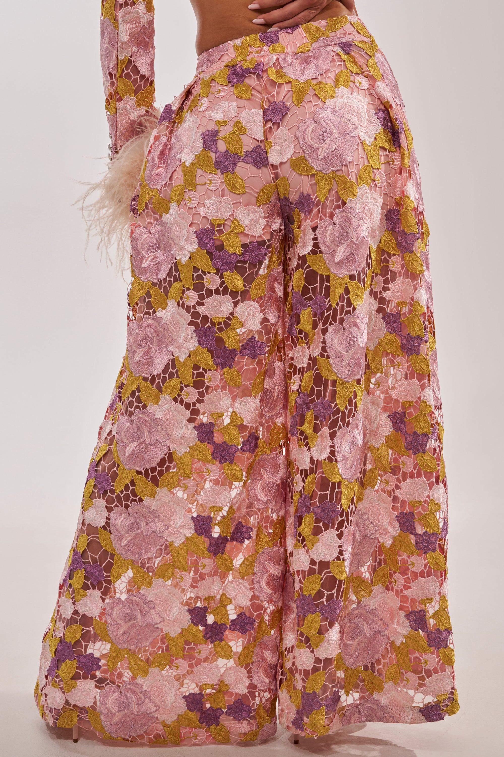 Someone wearing the LILA LACE PANT—vintage-luxe, wide-leg trousers crafted from sheer floral lace in pink, purple, and yellow with an intricate pattern and a soft, flowing texture. 6