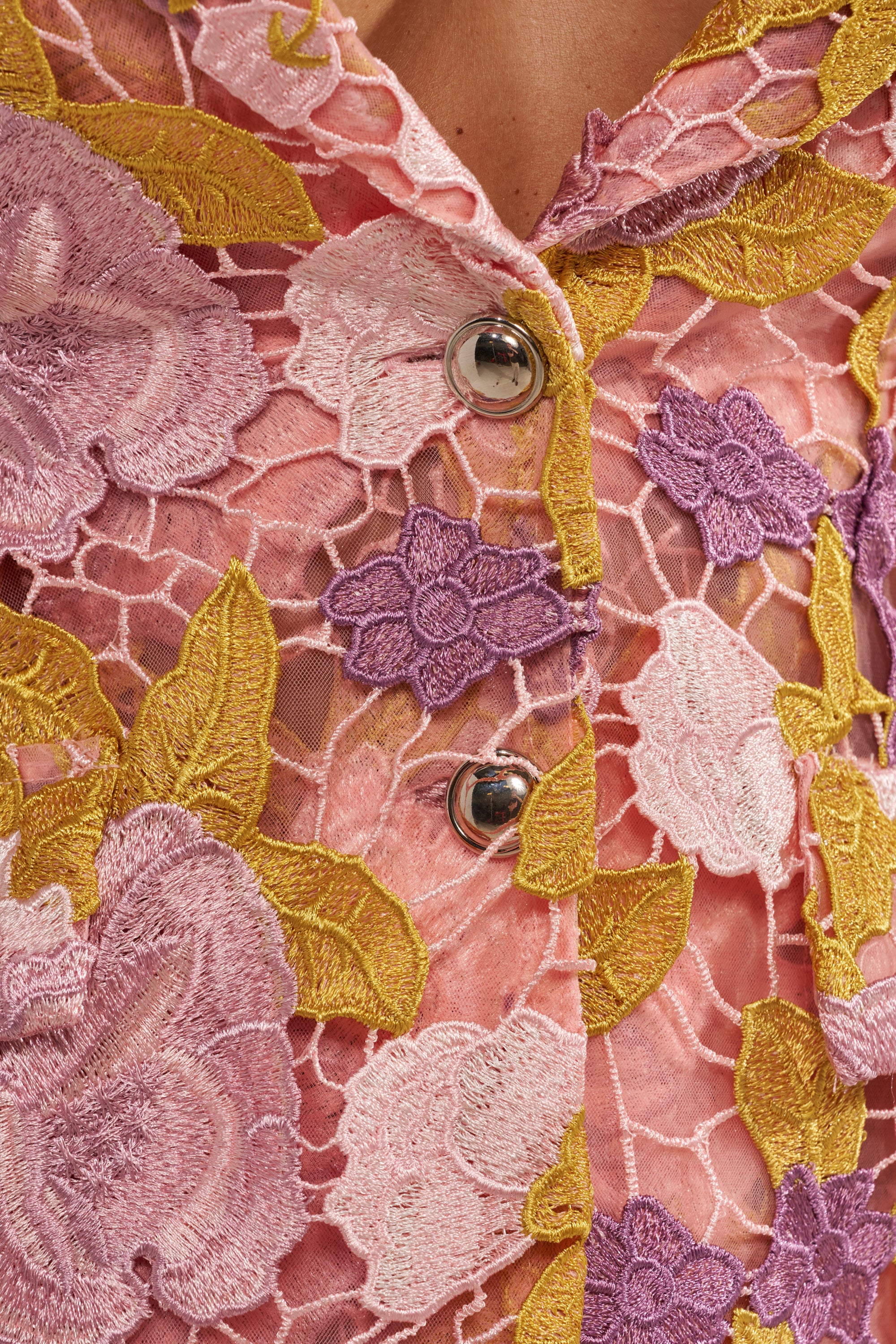 Close-up of the LILA LACE BLAZER in pink, featuring sheer lace with detailed floral embroidery in pink, purple, and yellow, finished with two metallic buttons. 8