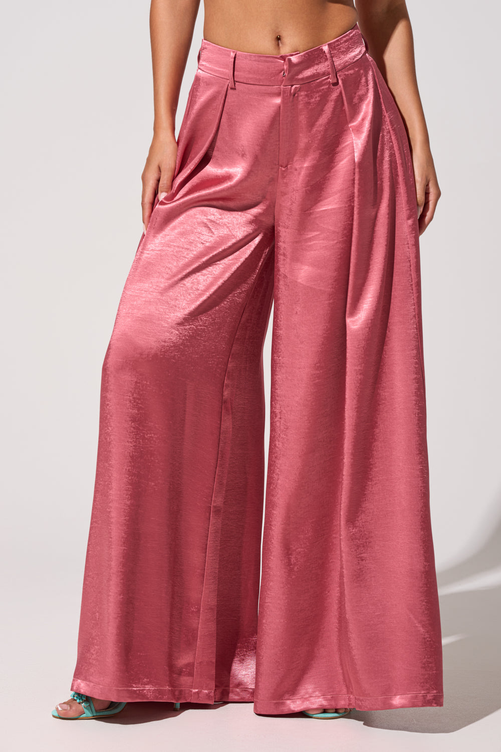 Wearing the IN FULL BLOOM TROUSER IN MAUVE, featuring high-rise satin, wide legs, pleats, belt loops, and pockets in a shiny pink shade. Only the lower body is visible against a plain light background. 2