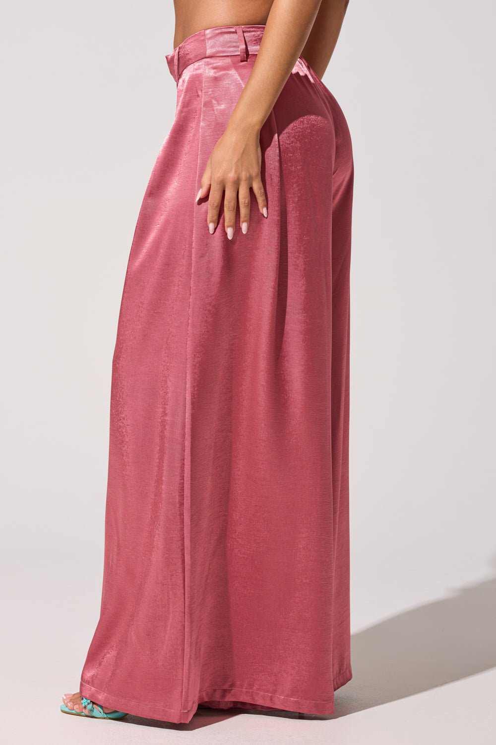Someone stands sideways against a plain light background, wearing the IN FULL BLOOM TROUSER IN MAUVE—high-rise satin wide-leg trousers with a matching belt. 4