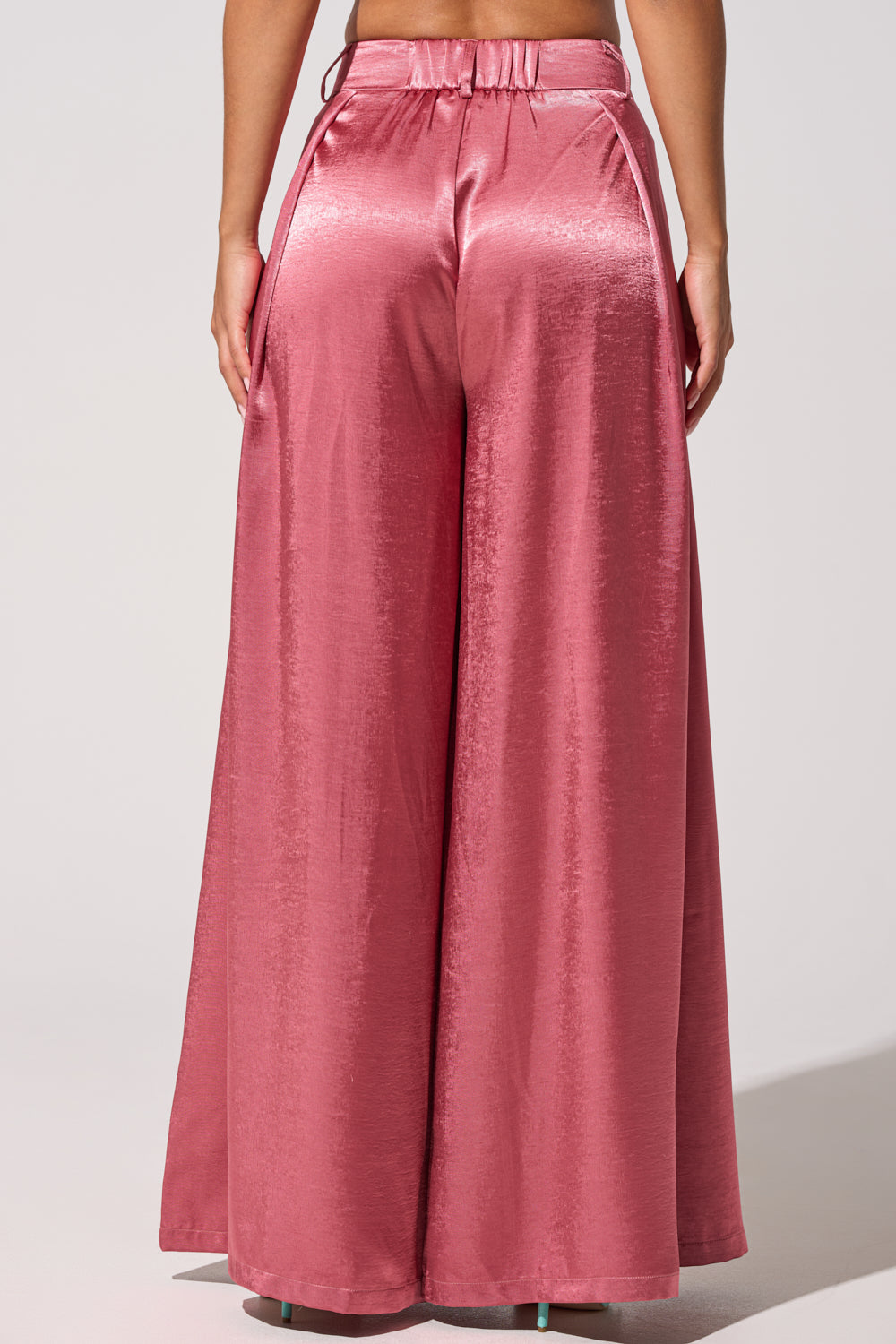 A person is seen from the back wearing the IN FULL BLOOM TROUSER IN MAUVE, featuring a high-rise fit, loose wide legs, visible seams, practical pockets, and a subtle satin sheen in shiny pink. 5