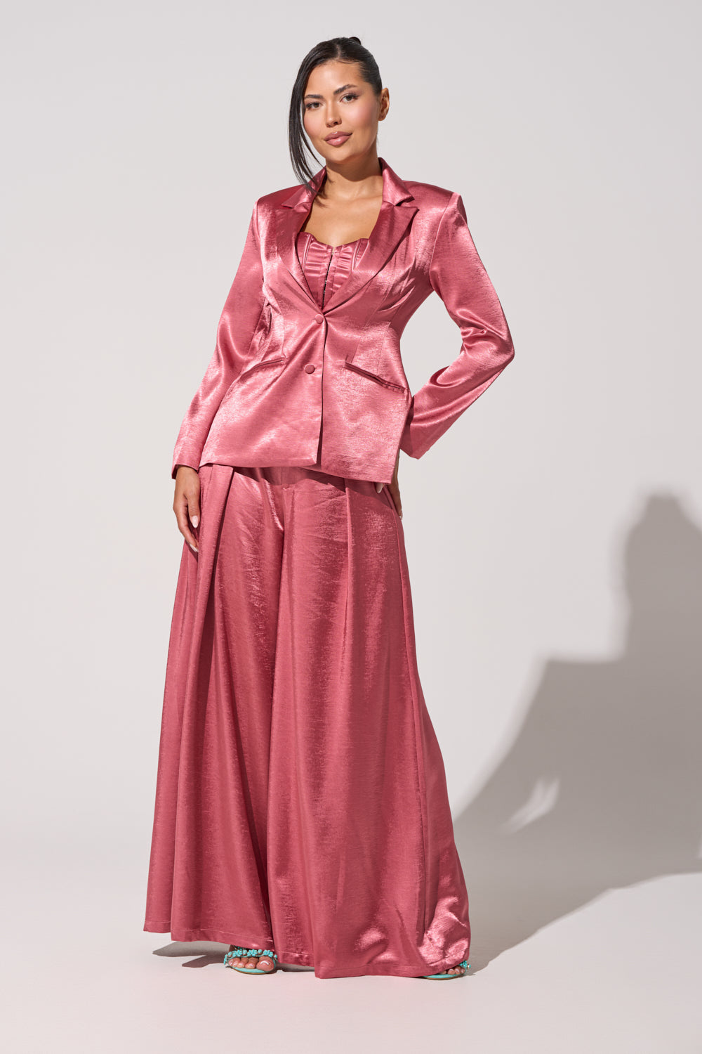 A woman poses confidently in the IN FULL BLOOM TROUSER IN MAUVE, featuring shiny mauve satin pants and a fitted blazer, against a plain light background. 7