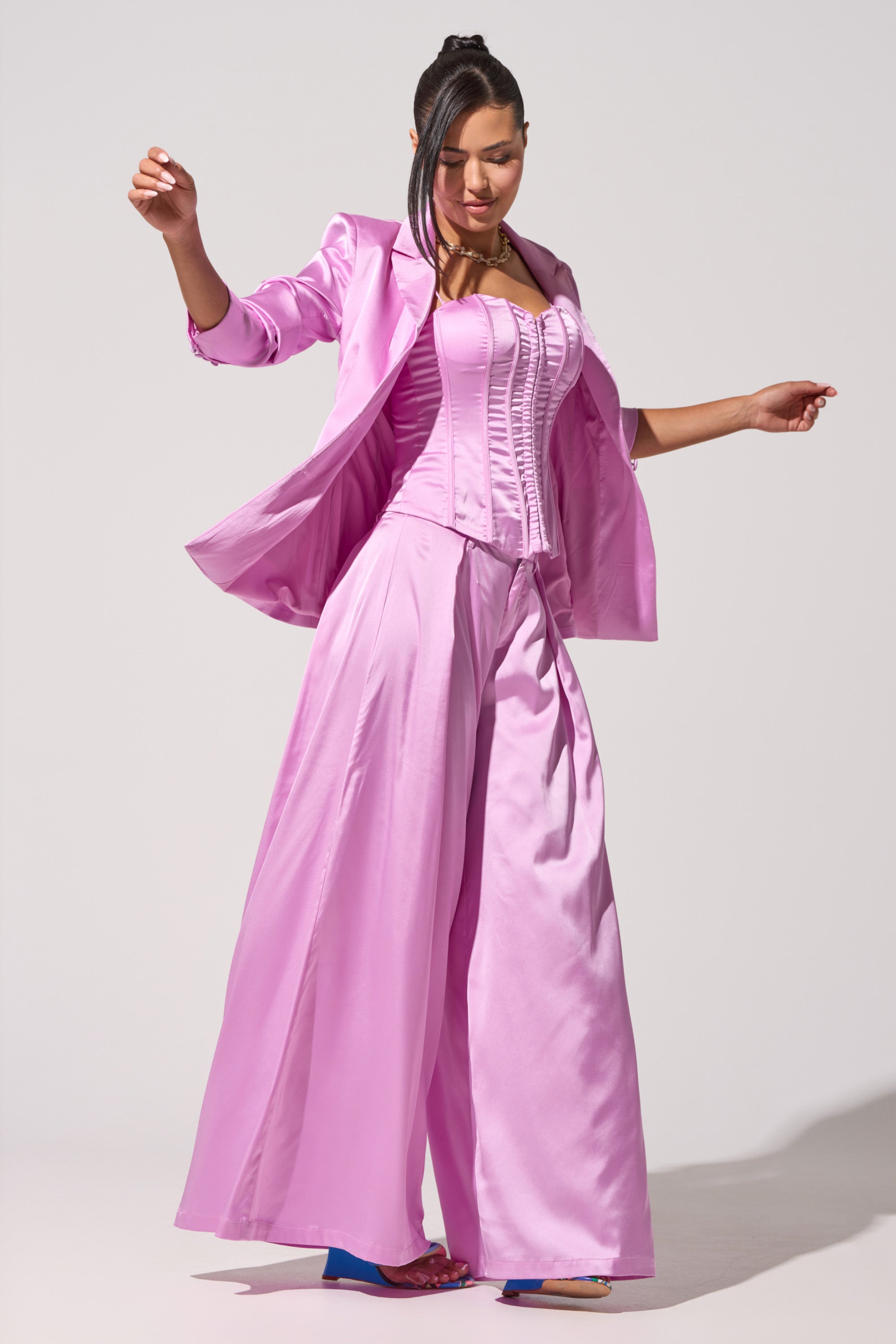 A woman with long dark hair poses against a plain light background in the IN FULL BLOOM LIGHT PURPLE TROUSER, featuring a chic high-rise waistband and wide-leg fit, styled with a matching corset top and blazer. 0