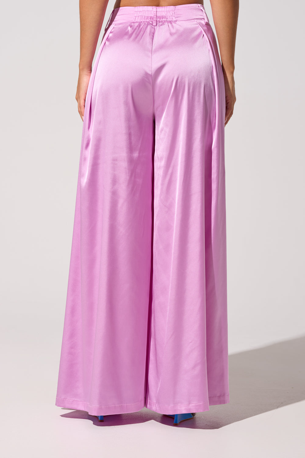 A person wears the IN FULL BLOOM LIGHT PURPLE TROUSER, shown from behind. The light purple satin pants feature a high-rise, loose fit and flowy fabric, captured against a plain, light background. 3