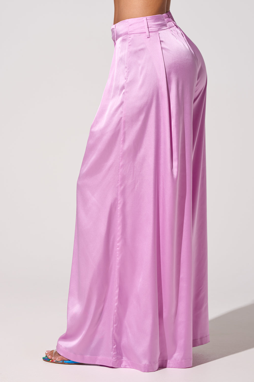 A person’s lower body is shown in side profile against a light background, wearing the IN FULL BLOOM LIGHT PURPLE TROUSER—satin, wide-leg tailored pants featuring front pleats. 4