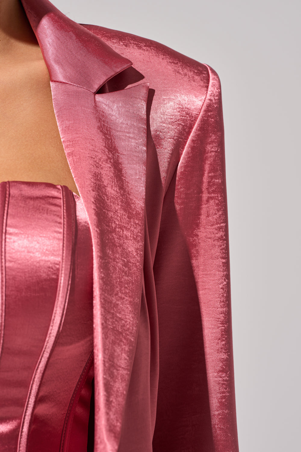 Close-up of a person wearing the IN FULL BLOOM BLAZER IN MAUVE draped over their shoulders, paired with a matching mauve strapless satin corset top, set against a plain background for an elegant power-suiting look. 7