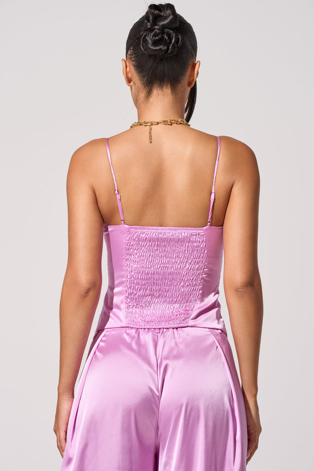 A woman with dark hair in an updo wears the IN FULL BLOOM LIGHT PURPLE CORSET, which features a shiny lilac satin finish and ruched detailing. She pairs it with a gold chain necklace and poses against a plain light background. 4