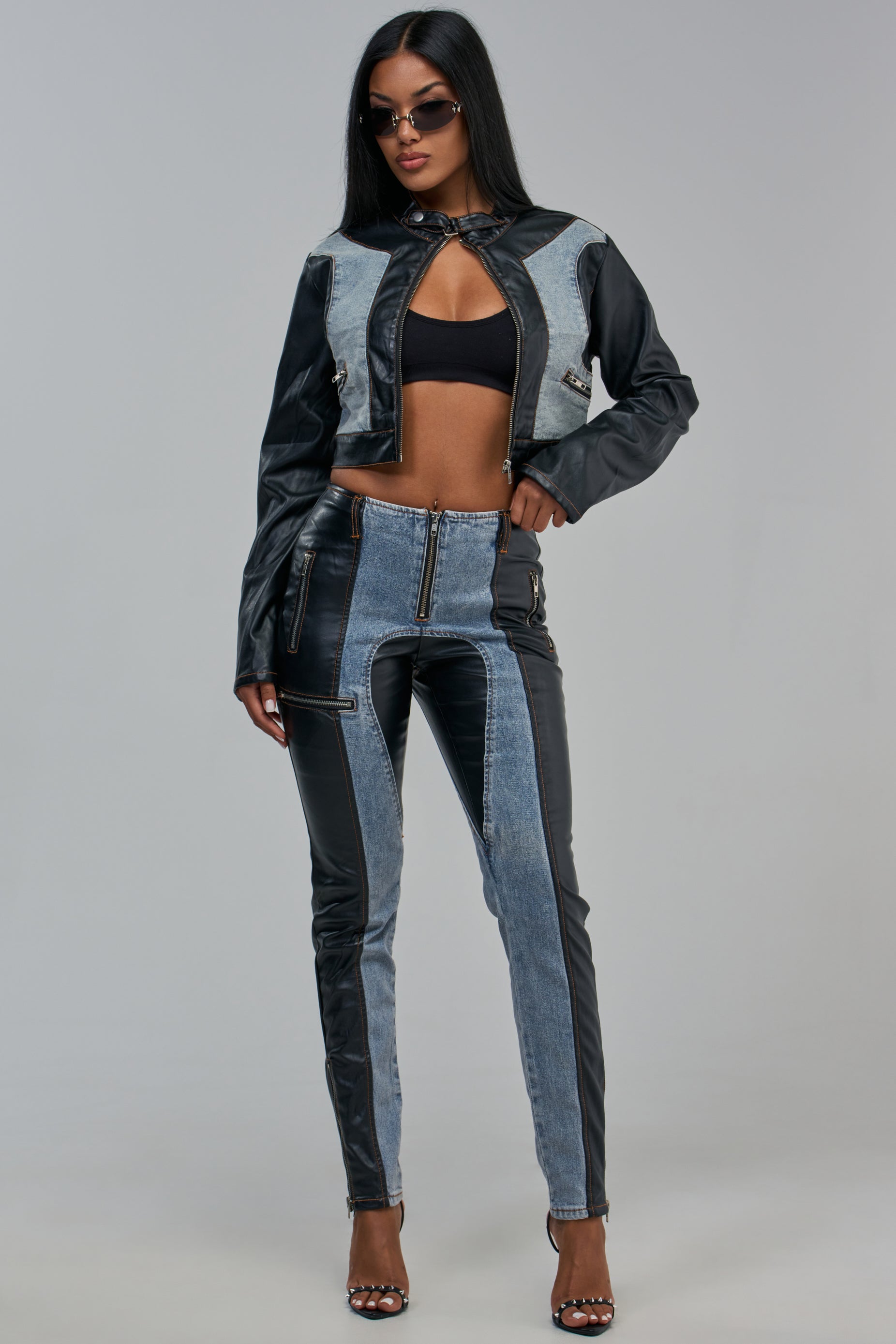 A person wearing a cropped jacket and the RACING TO THE FINISH DENIM MIXED WITH FAUX LEATHER TROUSER, both featuring a paneled design of denim and black faux leather.