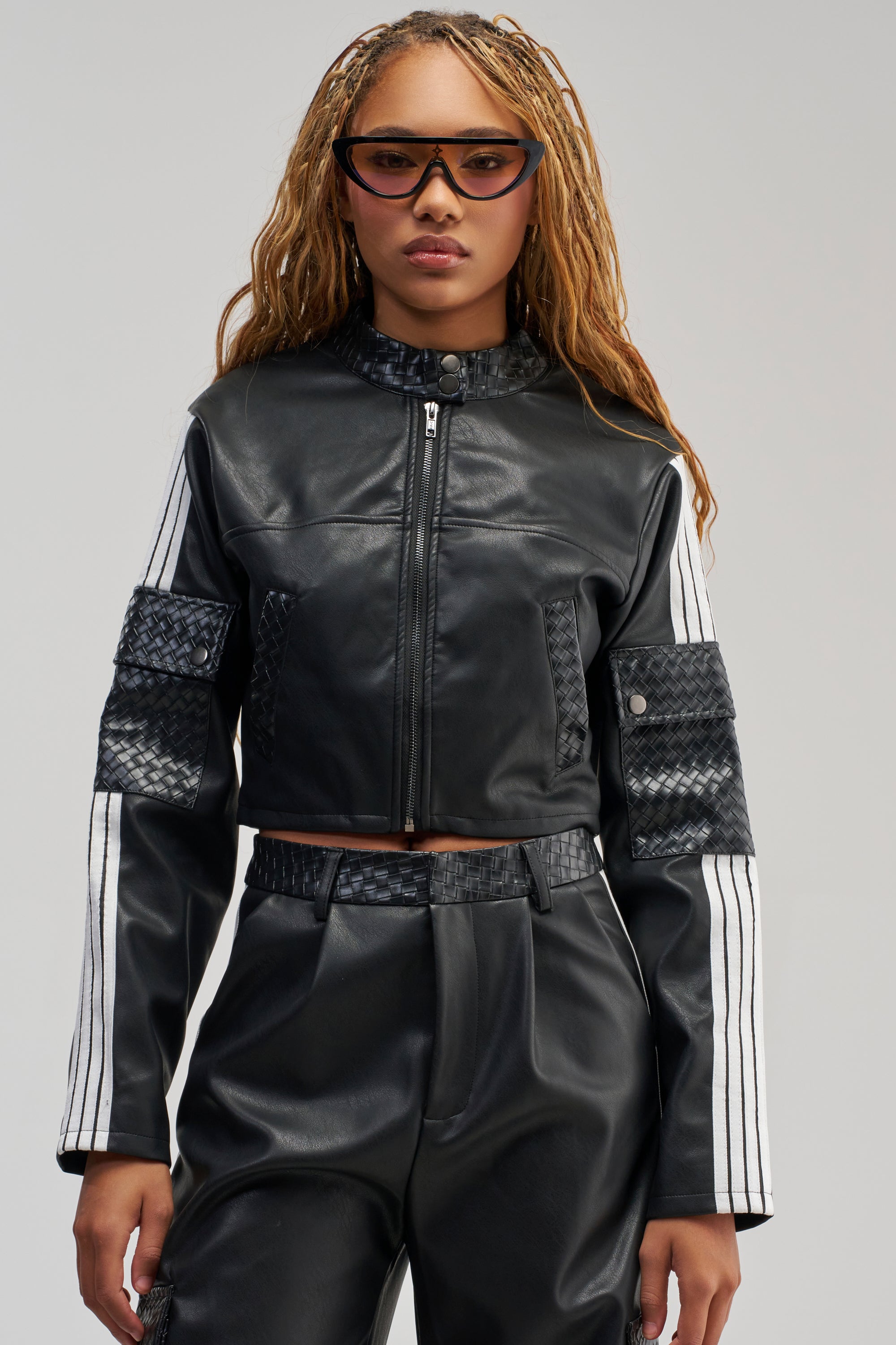 Wearing the DONT TEST ME FAUX LEATHER BOMBER, a person with matching pants and cat-eye sunglasses stands against a plain background.