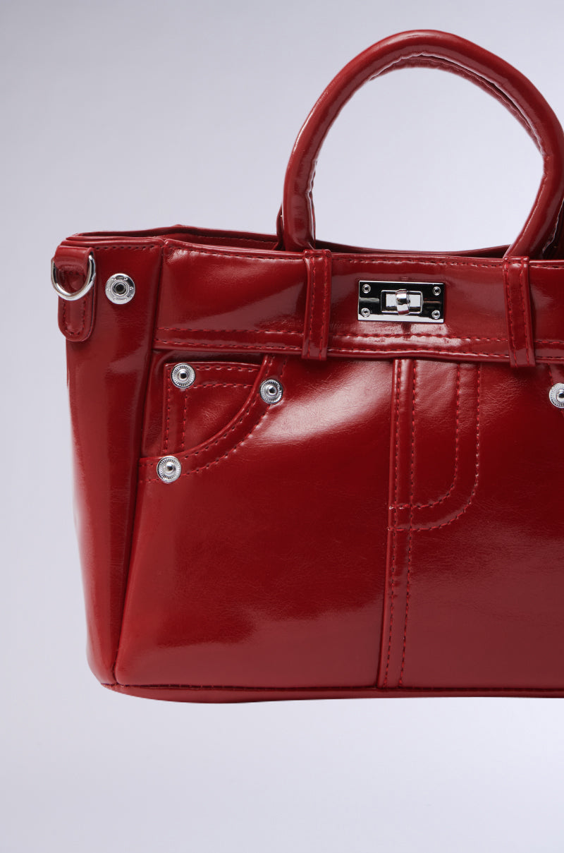 The TOP TIER PANTS PU PURSE, in striking red patent leather with metal studs and a twist-lock top closure, is showcased on a plain background. It features a structured design with short handles and decorative stitching, resembling a mini jacket with pockets and turn-lock details. 3