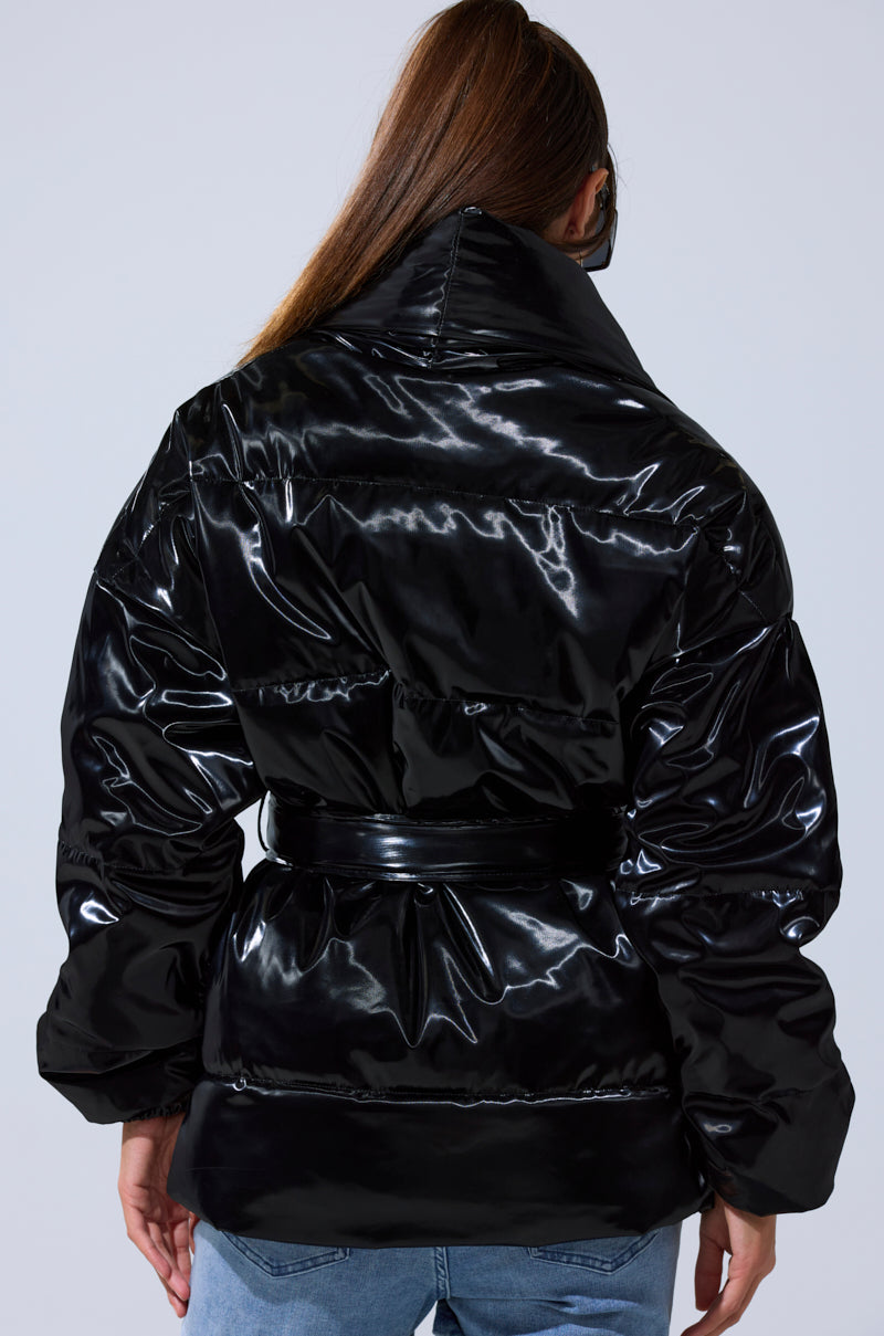 A person with long brown hair, seen from behind, models the LIQUID METAL WRAP PUFFER with a belt and blue jeans against a plain light gray background.
