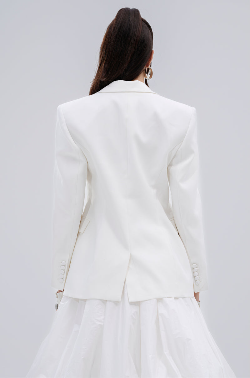 A person with long dark hair wears the PERFECT FIT BLAZER and a voluminous white skirt made from sleek suiting material, shown from the back against a light gray background.
