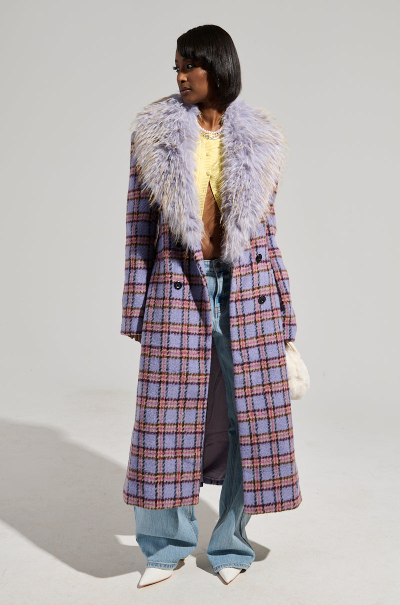 Dressed in the TEA FOR TWO FUR TRIM TRENCH, which features a plush light-colored fur trim and luxe satin interior lining, an individual pairs it with a vibrant yellow top, classic blue jeans, and sleek white pointed shoes. They accessorize with a small fuzzy bag and pose against a simple backdrop.