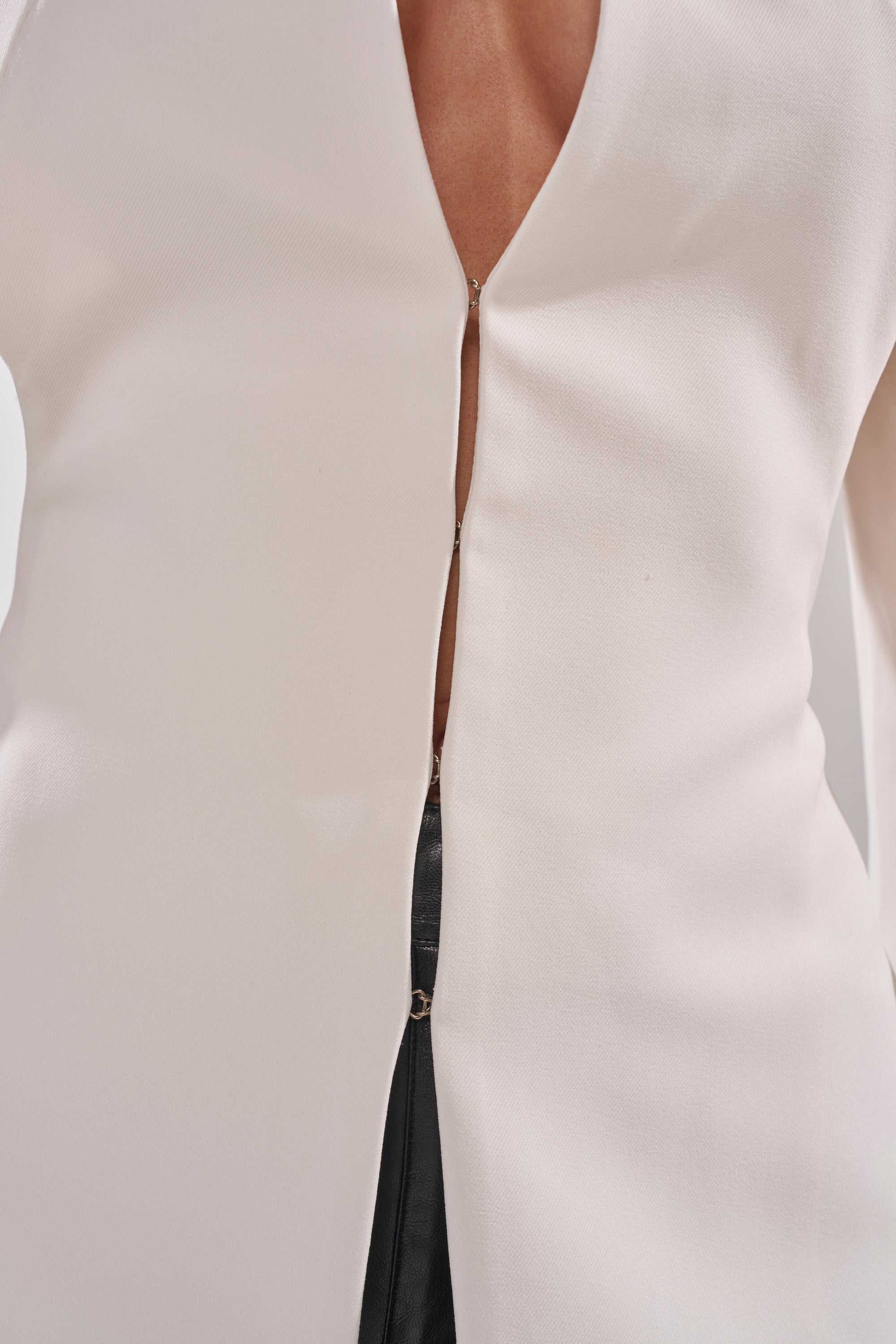 A close-up of a person wearing the WHEREVER YOU ARE CUTOUT TRENCH IN WHITE over a cream V-neck top with a front zipper, paired with black pants. 6