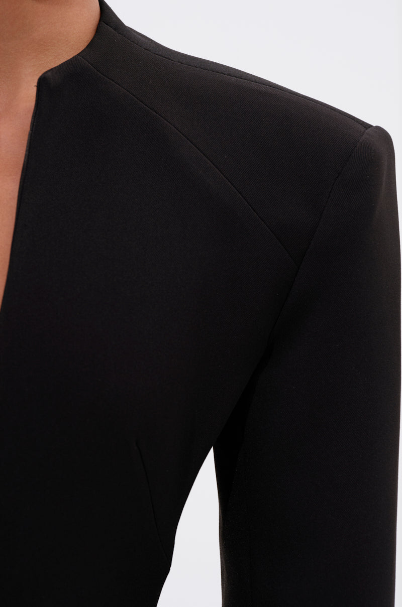 Close-up of a person wearing the WHEREVER YOU ARE CUTOUT TRENCH, a tailored black blazer with sharp shoulders and a deep V-neckline, styled like a longline coat, against a plain light background.