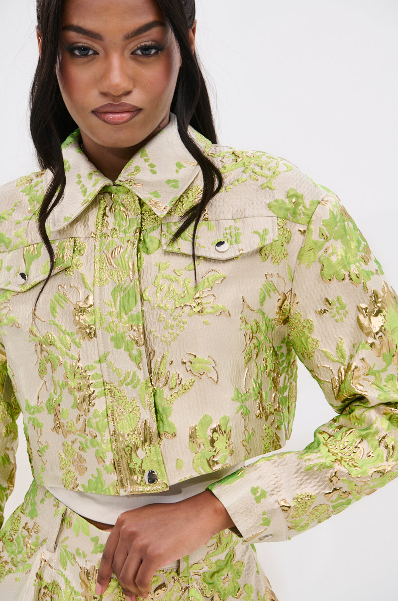 A woman models the HOT SHOT BROCADE BOMBER, a cream cropped jacket with metallic gold and light green floral brocade, standing before a plain white background.