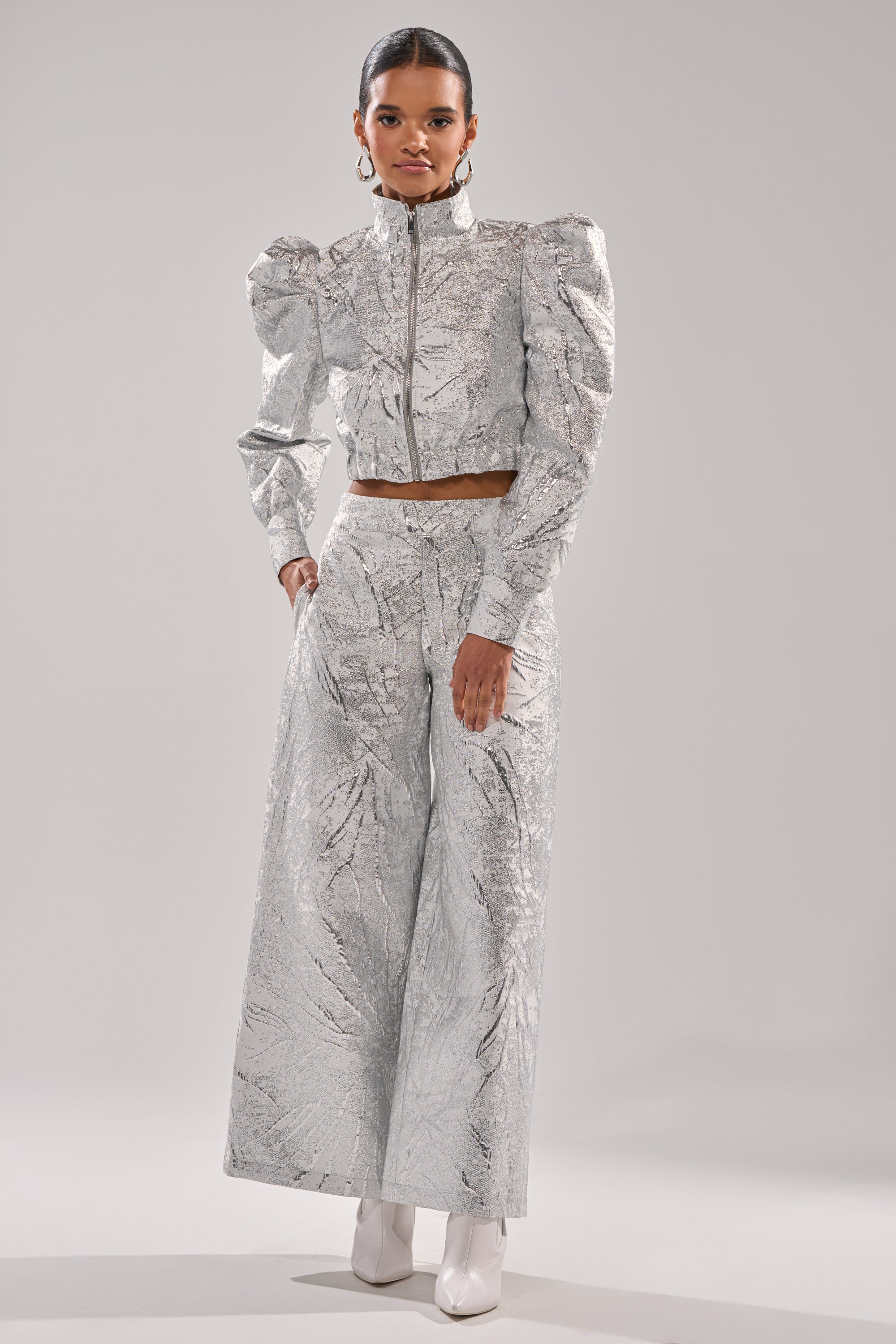 A person stands confidently in the JUST LIKE THAT BROCADE BOMBER with puffed shoulders, matching wide-leg pants, and white ankle boots against a plain light background. 6