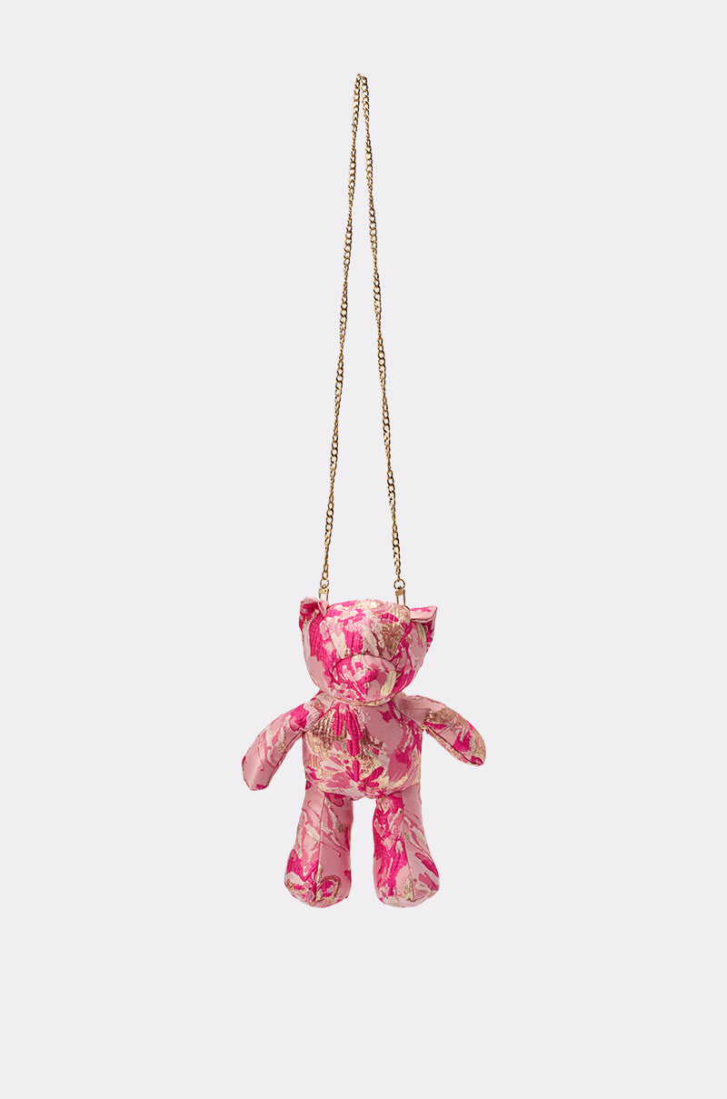The REALLY ME BROCADE BEAR BAG, a small pink teddy bear-shaped crossbody with a pink and white floral pattern and gold chain strap, is displayed against a plain light background. 1