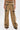 Wearing the EAST HAMPTON WIDE LEG TROUSERS IN BROWN, featuring a mid-rise fit, black faux leather piping, decorative zippers, and gold button flap pockets, styled with open-toe black sandals.