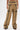 A person models the EAST HAMPTON WIDE LEG TROUSERS IN BROWN with black faux leather piping, zippers, and flap pockets, styled with black open-toe heels. The high-waisted tan pants are the focus of this cropped lower-body shot.