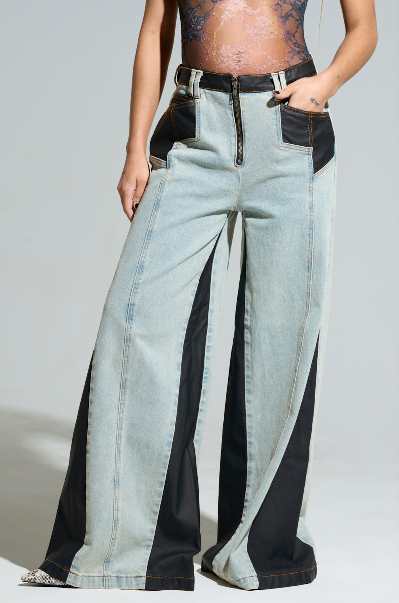 Wearing the WILL COLORBLOCK WIDE LEG JEAN, which features high-waisted black faux leather panels, exposed stitching, and zipper and buckle details at the waist, paired with a lace-patterned top.