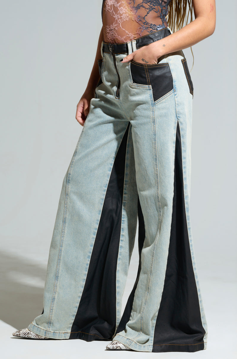 A person wearing the WILL COLORBLOCK WIDE LEG JEAN, which features high-waisted wide-leg design with colorblock black panels on the sides, paired with a lace top. The jeans include large side slits that reveal contrasting fabric underneath, creating a stylish and modern look.