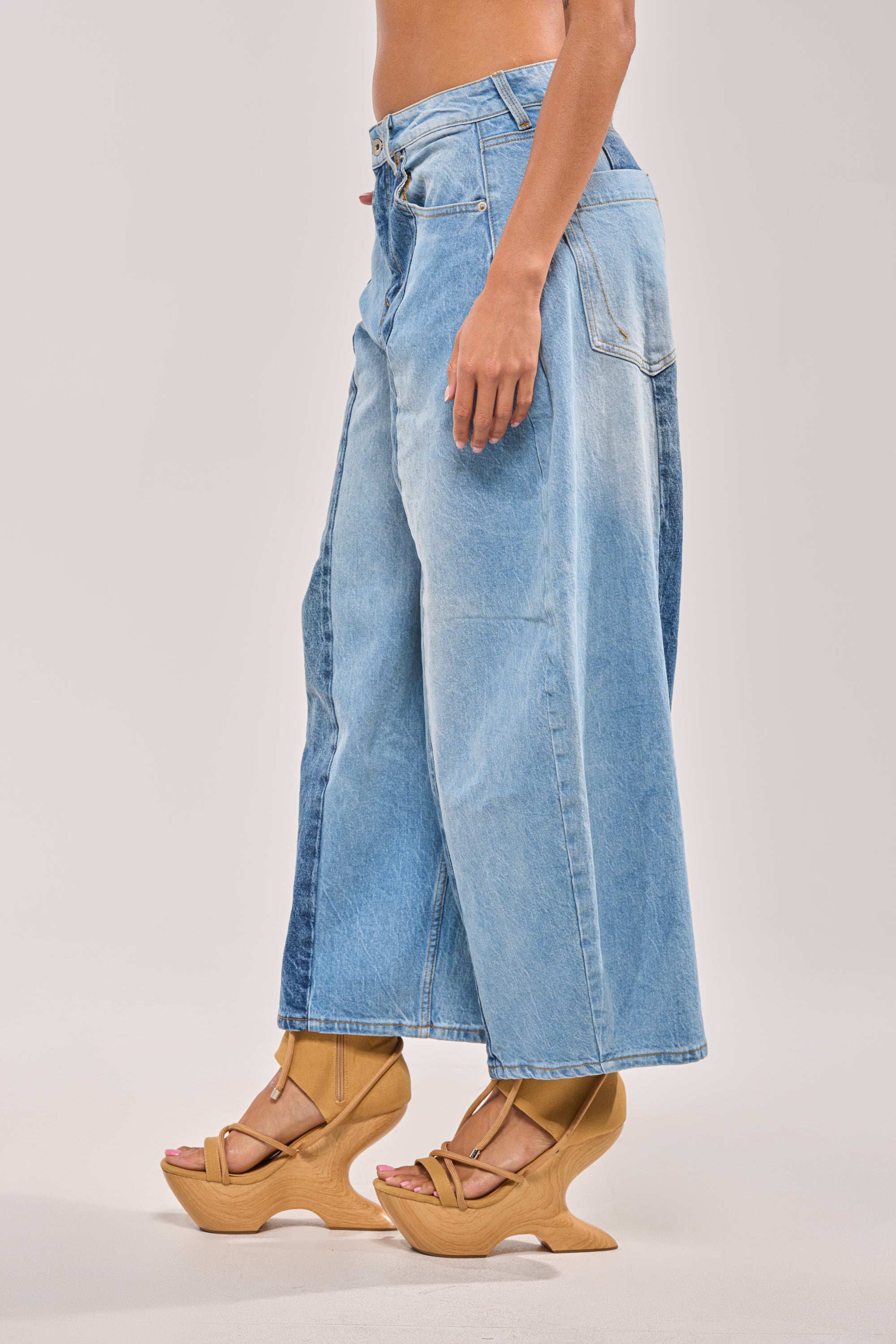 A person wearing MIXED EMOTIONS COLORBLOCKED BARREL DENIM, featuring wide legs and a high-rise fit, paired with tan wooden platform sandals, stands sideways against a plain background. 2