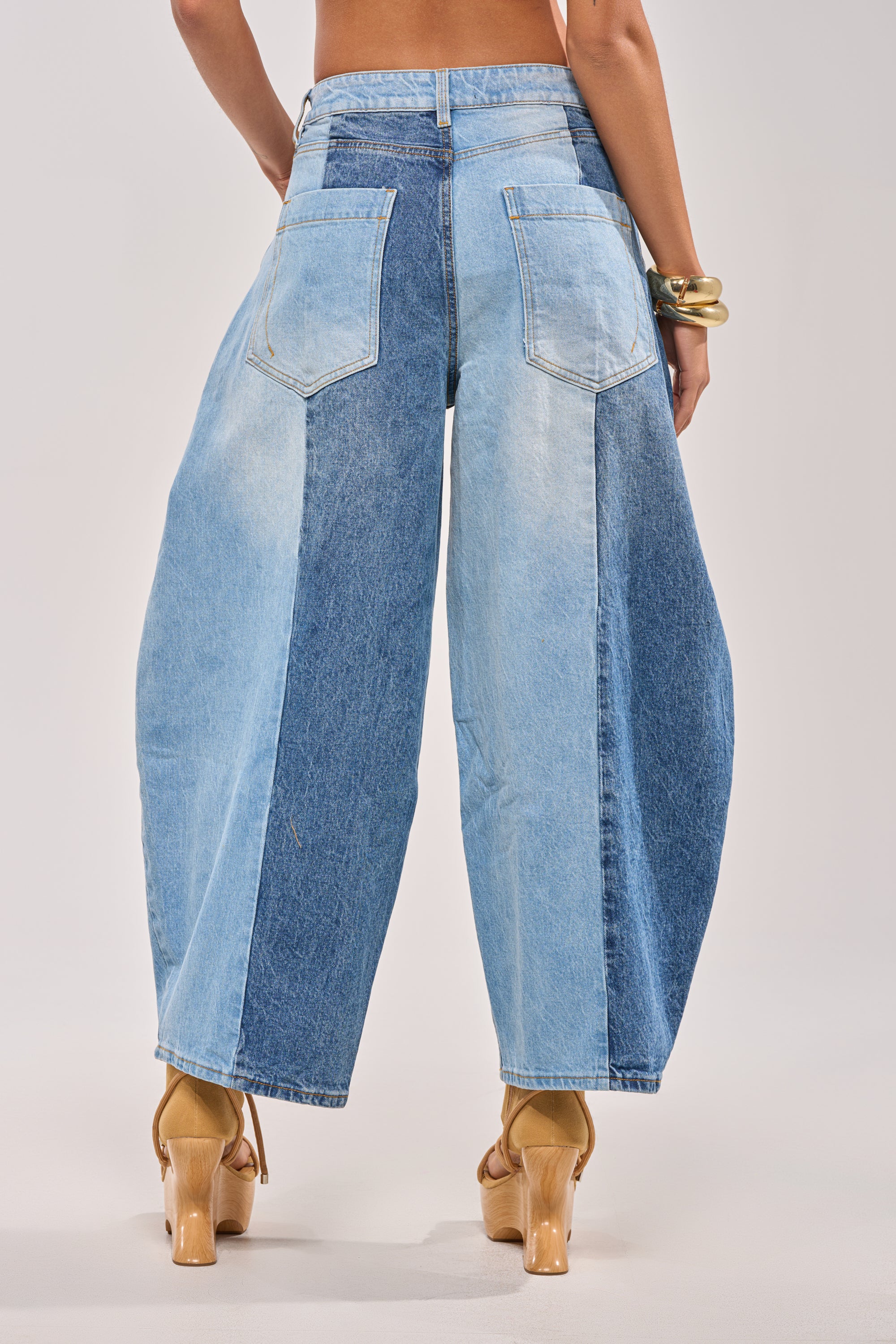 Someone is photographed from the back against a plain background wearing the MIXED EMOTIONS COLORBLOCKED BARREL DENIM with large back pockets, nude high-heeled sandals, and a chunky gold bracelet. 4