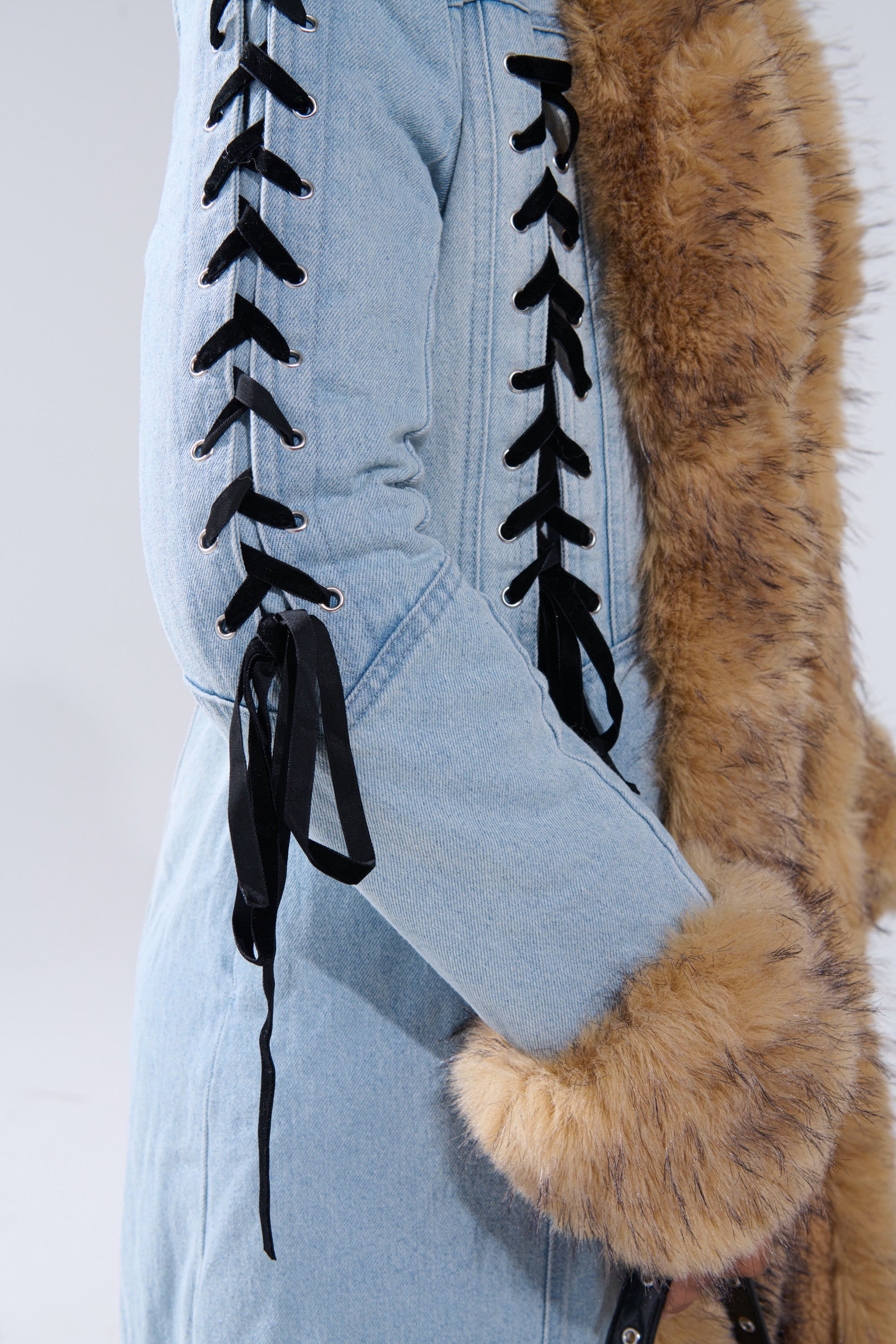 The ERYKAH FUR TRIM DENIM TRENCH features black ribbon lace-up sleeves and tan faux fur on the collar and cuffs. This sherpa-lined longline coat is modeled against a plain background.