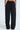 Someone is wearing the FEELING CUTE BOW DETAIL PANT with an elastic waistband, shown from behind. These black pants have a wide-leg style and white bows lining each side, set against a plain light background.