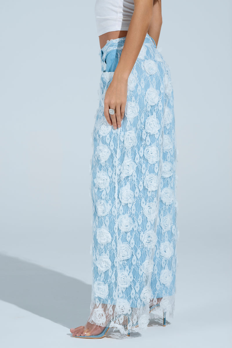 A woman in a white sleeveless top and FOLLOW MY LEAD APPLIQUE WIDE LEG DENIM is shown from the side, standing barefoot against a plain light blue background.