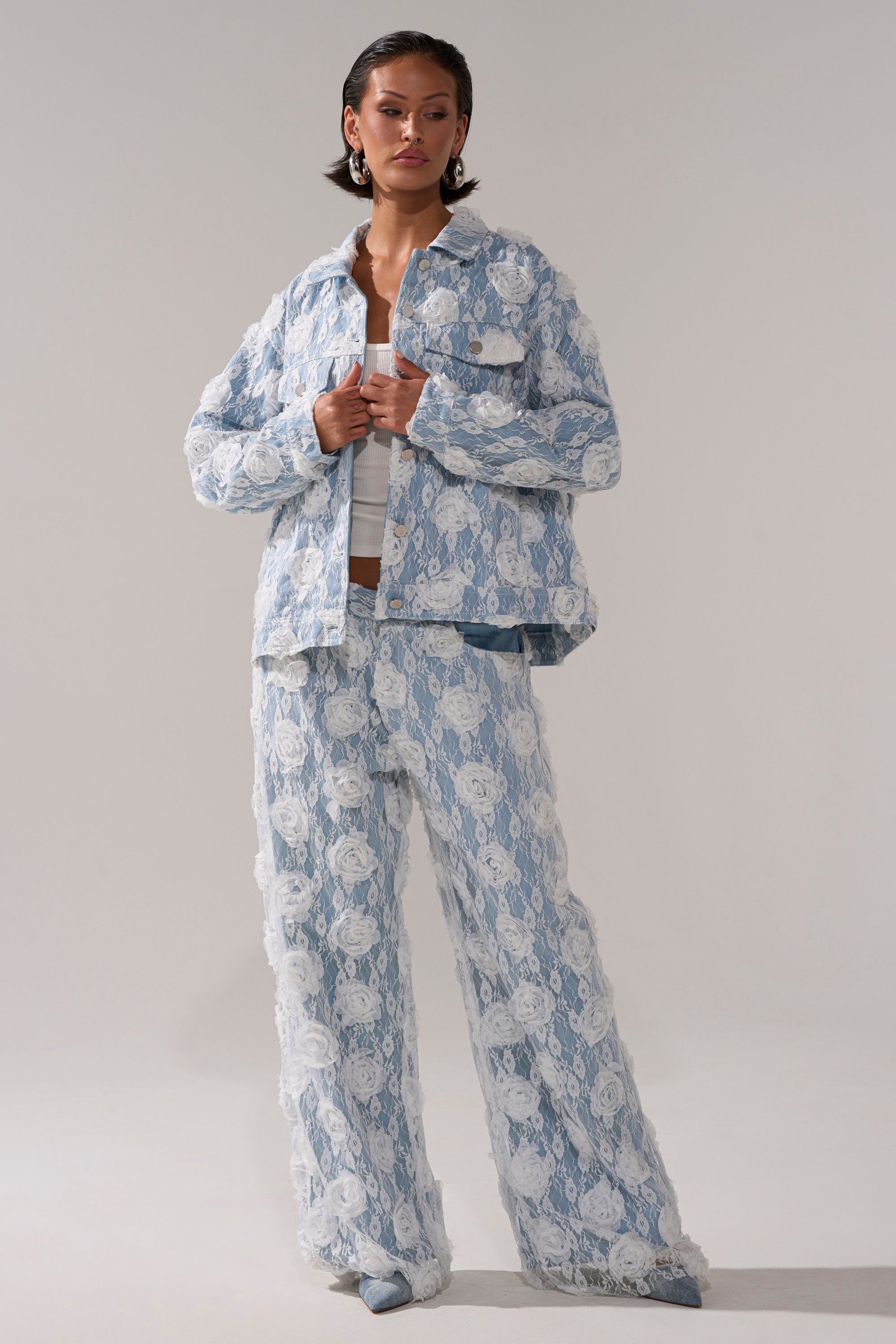 A woman wears the FOLLOW MY LEAD APPLIQUE WIDE LEG DENIM with a matching light blue and white lace-textured jacket over a white top, posing confidently against a plain light gray background.