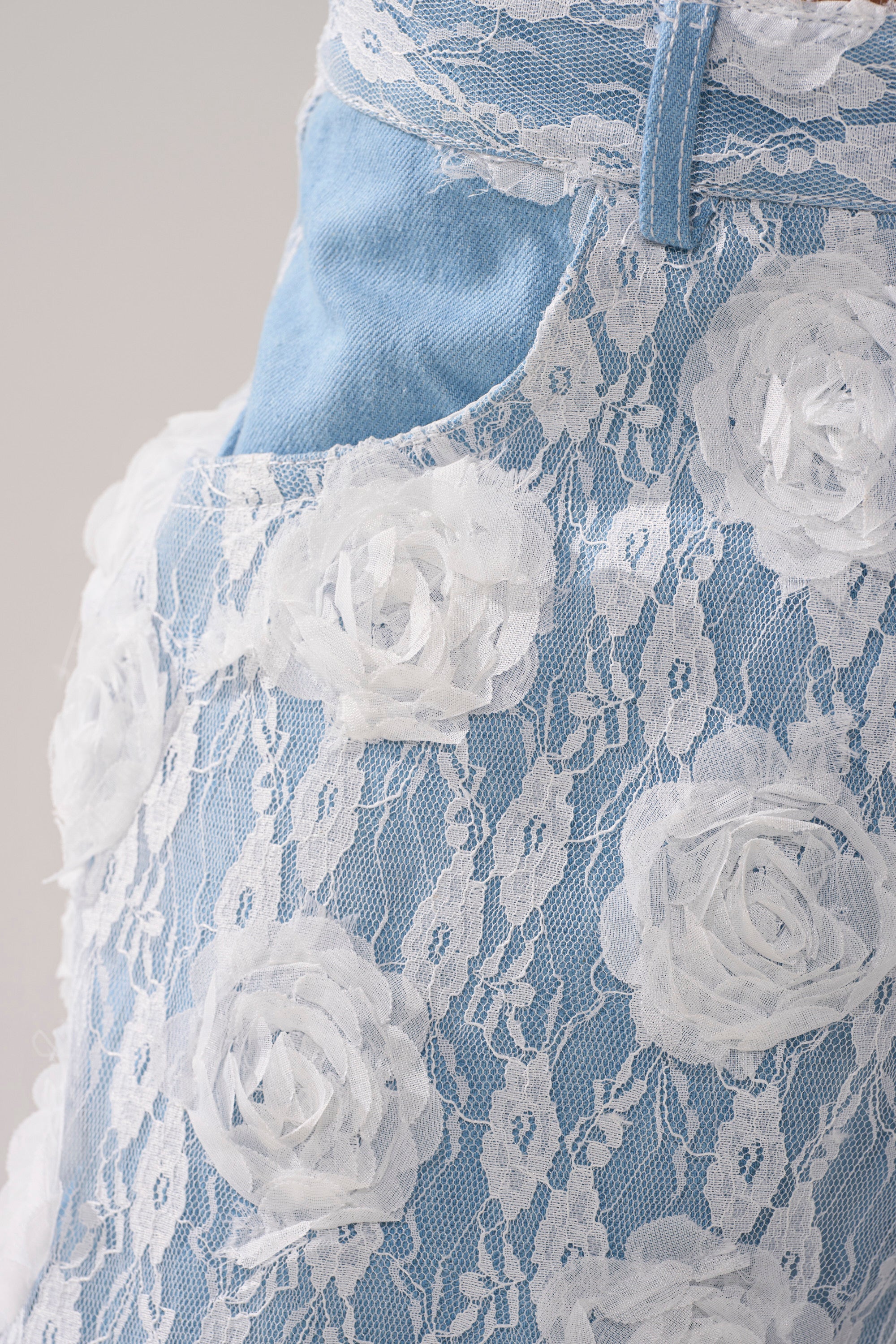 Close-up of the FOLLOW MY LEAD APPLIQUE WIDE LEG DENIM in light blue, featuring white floral lace and rosette appliqué, with a pocket detailed by a delicate lace overlay.