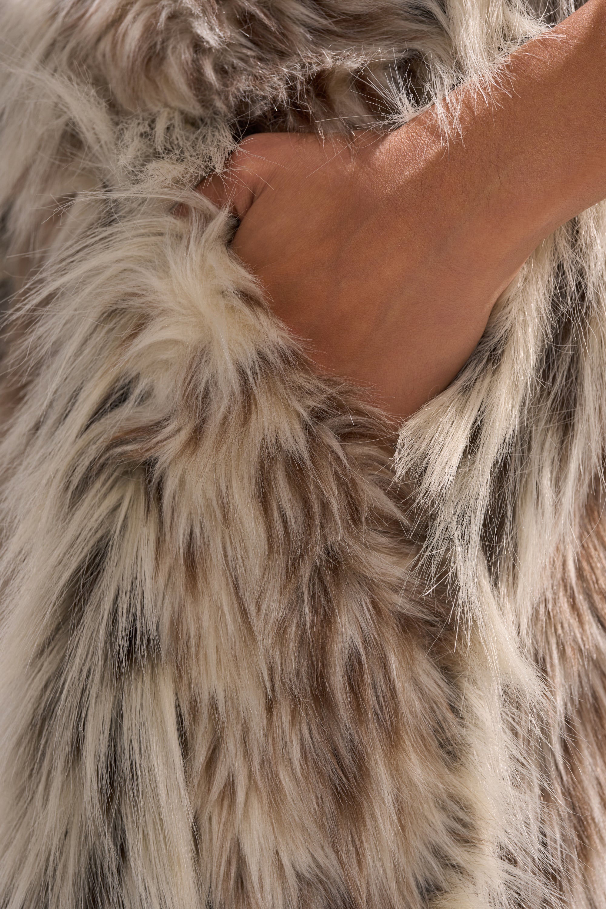A hand tucked into the pocket of PARTICULAR TASTE FAUX FUR CARGO PANTS, crafted from thick, multi-colored faux fur in shades of brown, gray, and white.
